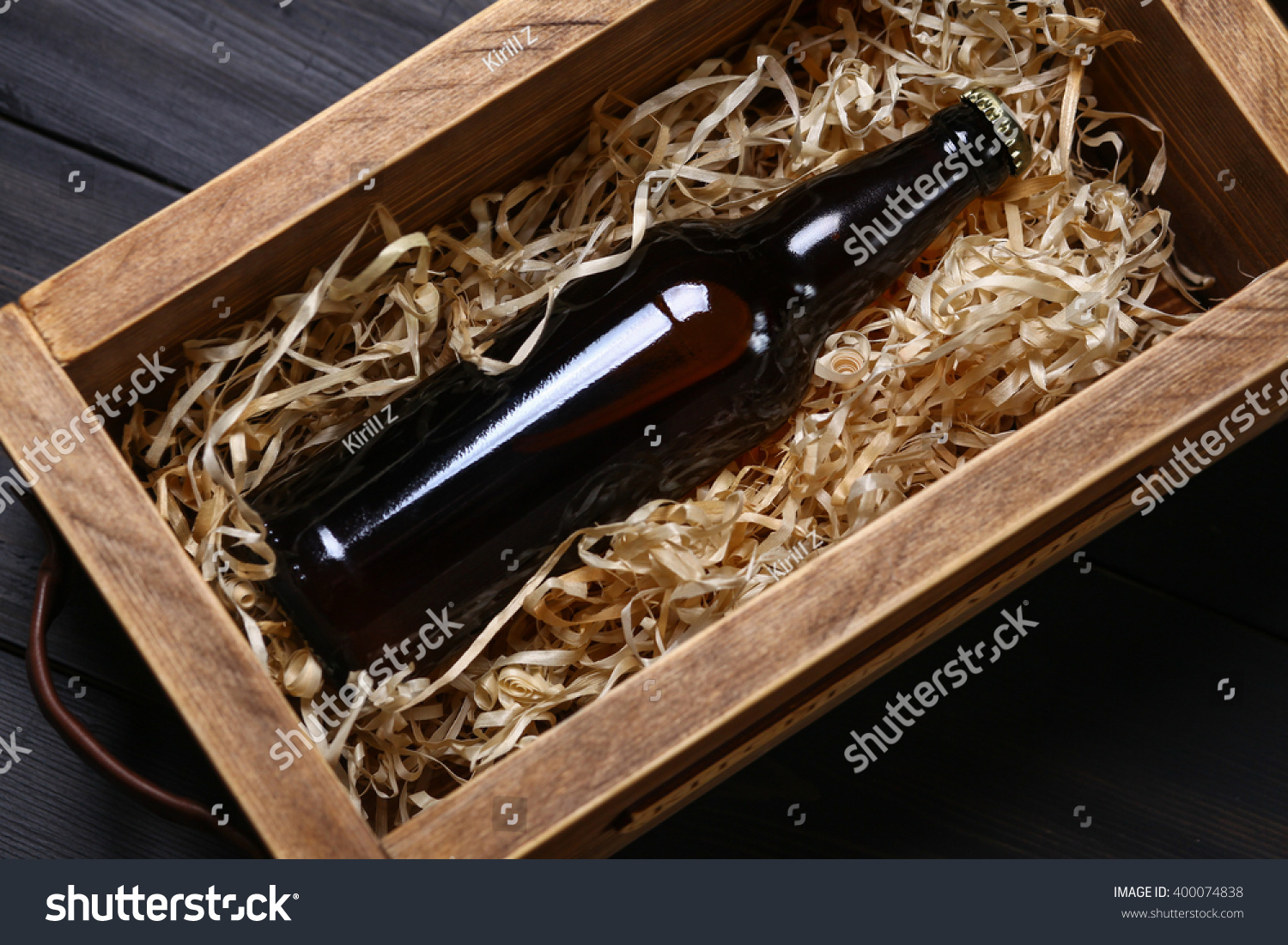 Bottle of beer in a wooden crate with wood shavings on a dark wooden surface #400074838