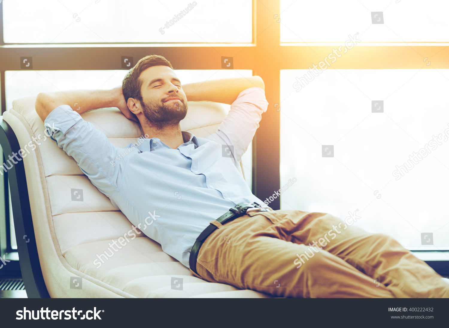 Time to relax. Handsome young man holding hands behind head while sleeping on the couch #400222432