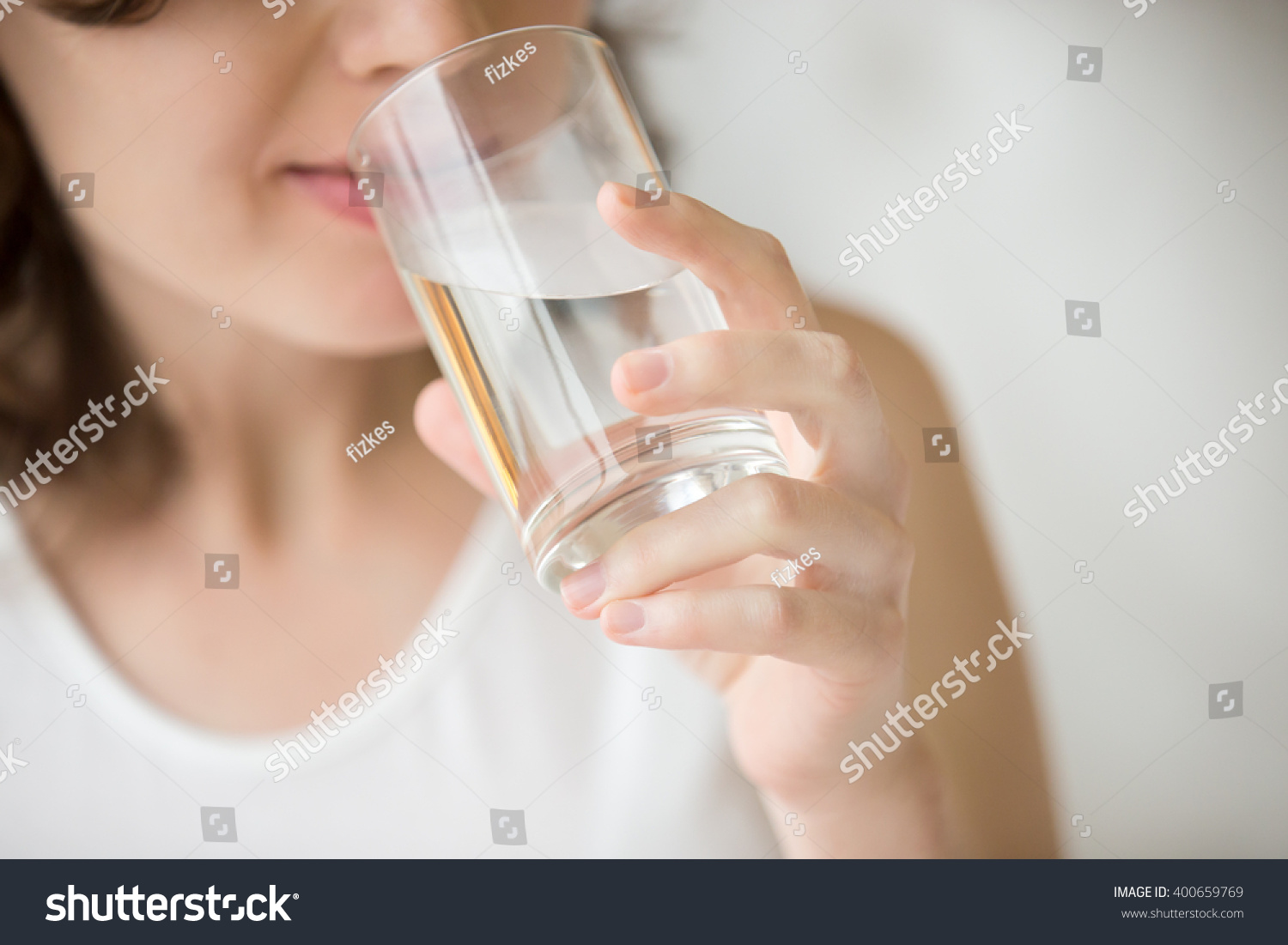 Happy beautiful young woman drinking water. Smiling caucasian female model holding transparent glass in her hand. Closeup. Focus on the arm #400659769