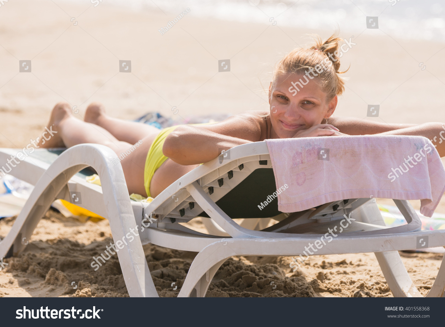 Young girl lying on a sun lounger on the beach with a smile looks in the frame #401558368