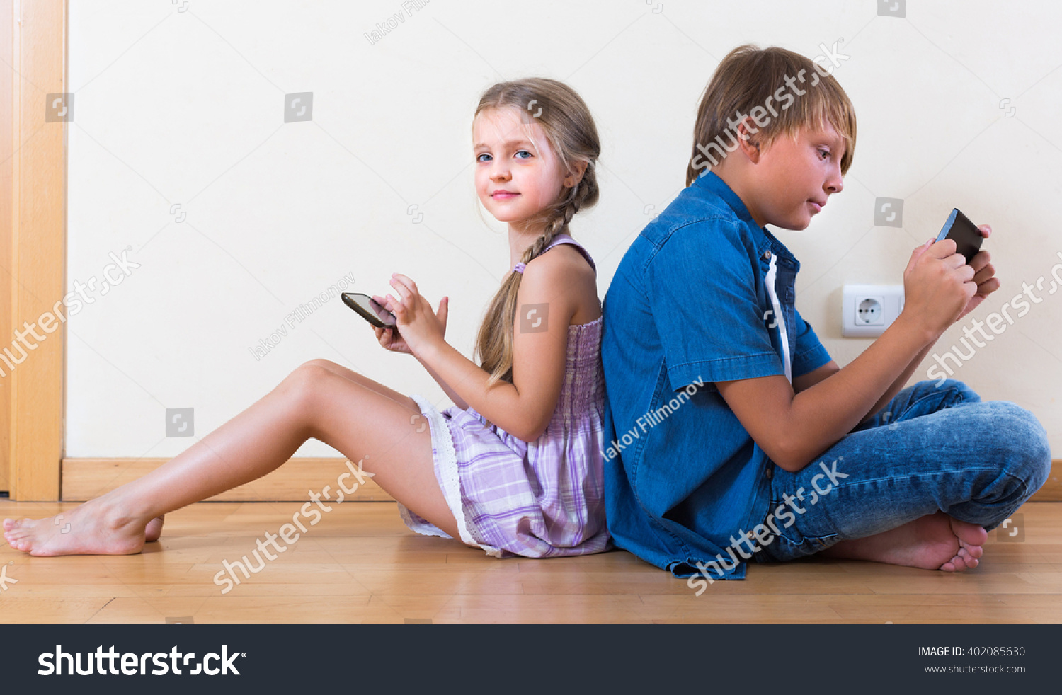 Little girl and teenage boy burying in mobile phones sitting on the floor
 #402085630