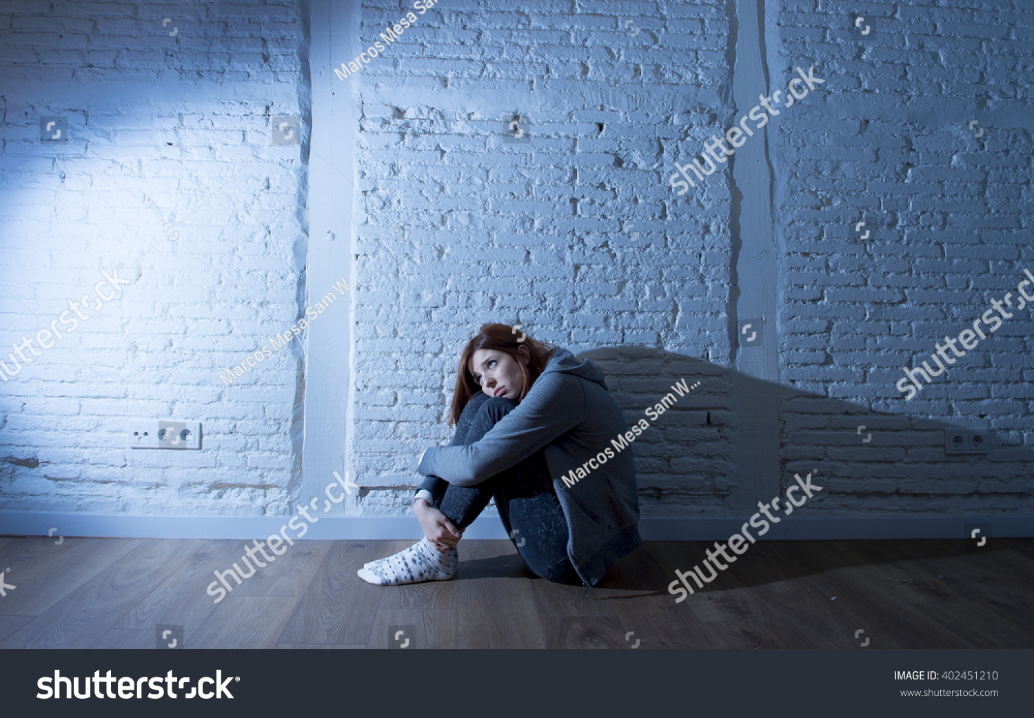teenager girl or young woman with red hair feeling sad and scared looking overwhelmed and depressed sitting on home floor in youth depression and suffering  problem in harsh contrast light #402451210