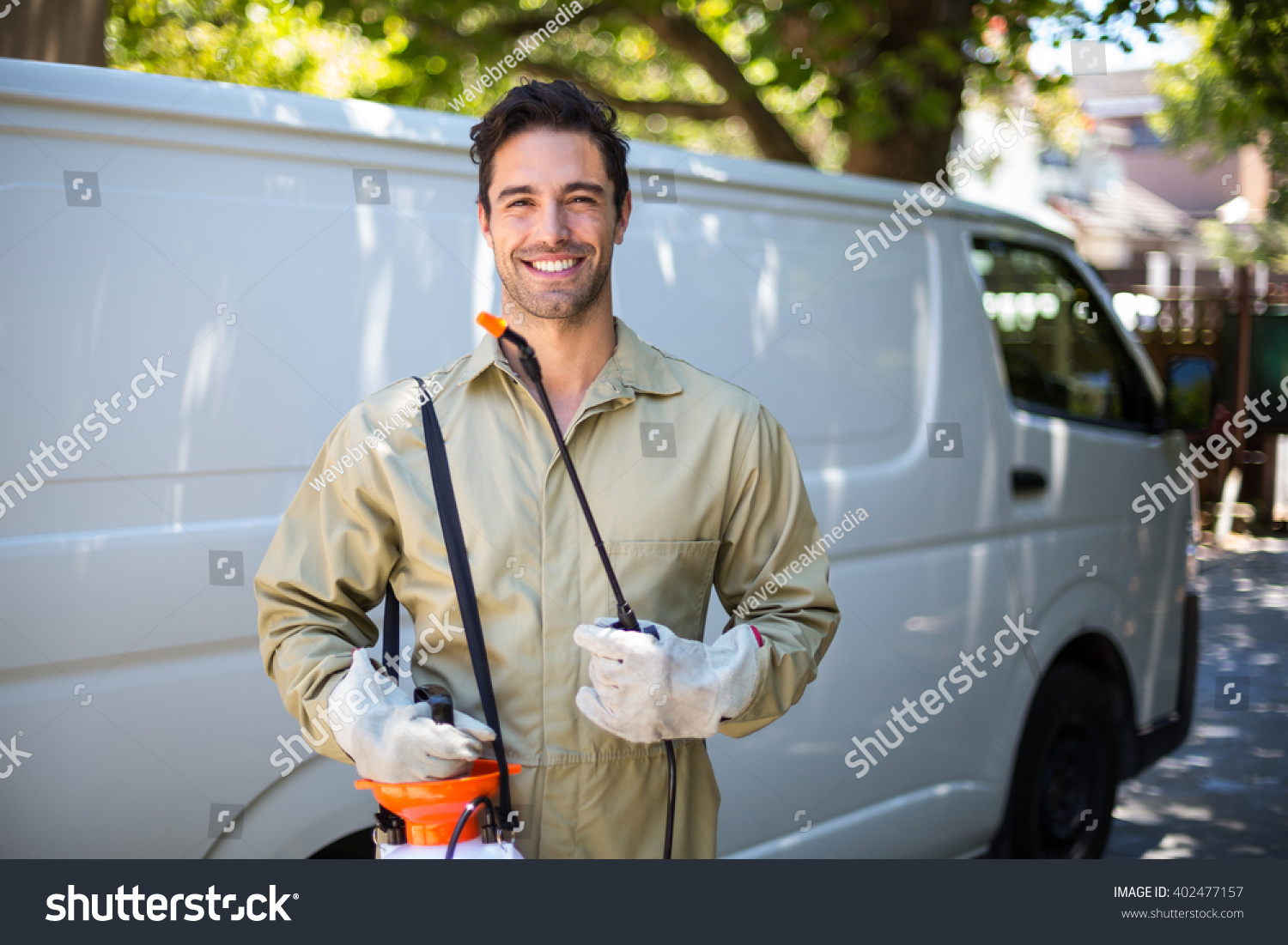 Portrait of smiling worker with pesticide sprayer while standing by van #402477157