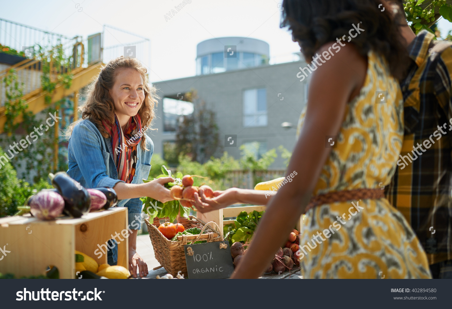 Friendly woman tending an organic vegetable stall at a farmer's market and selling fresh vegetables from the rooftop garden #402894580
