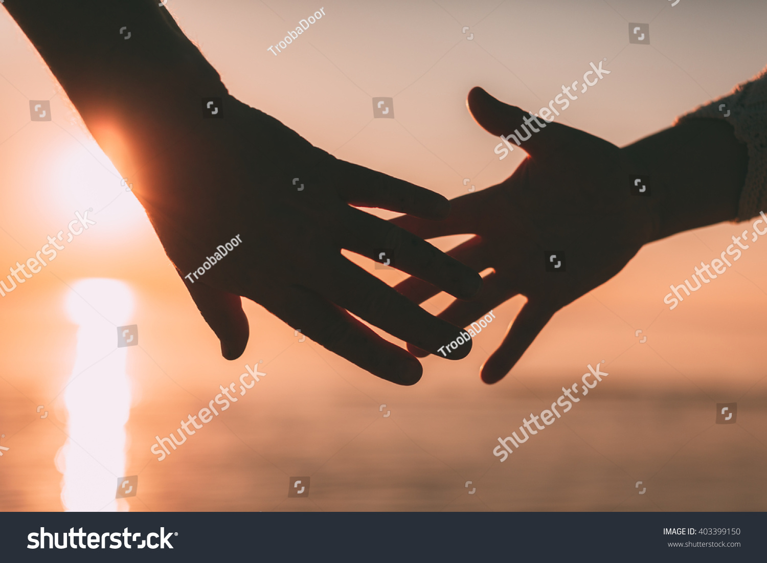 Couple hands reach silhouette on a sky and sea background. Evening photo. #403399150