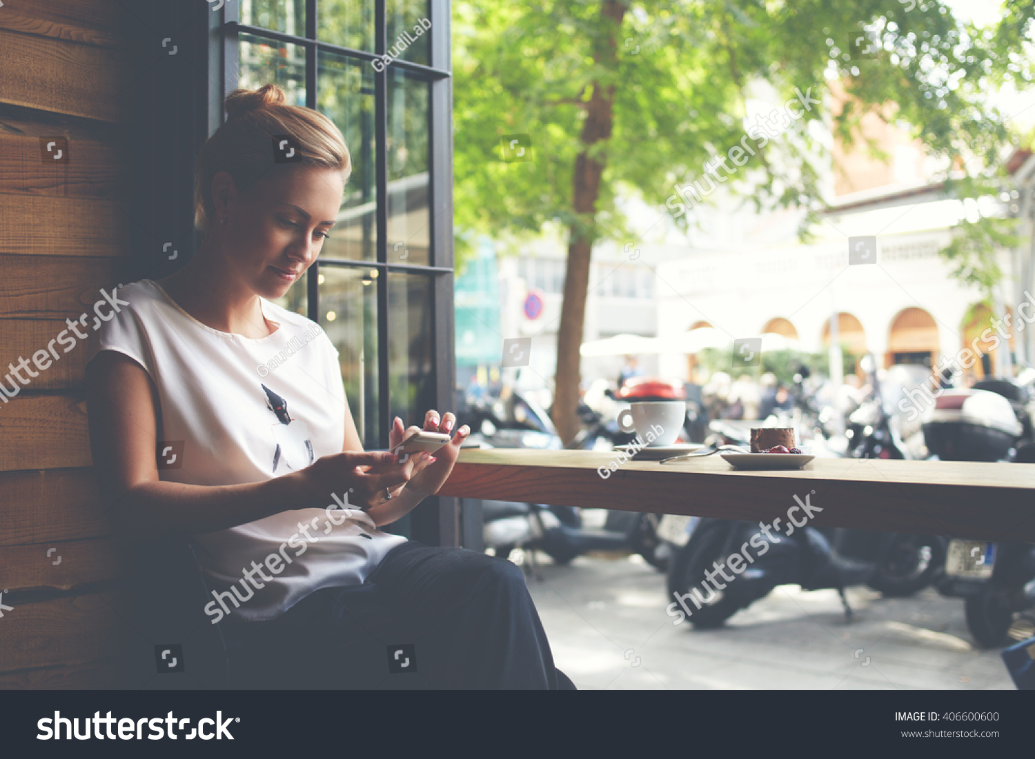 Young gorgeous lady chatting on her smart phone while relaxing in cafe after walking during summer weekend, attractive woman reading text message on cell telephone while sitting in cozy coffee shop  #406600600
