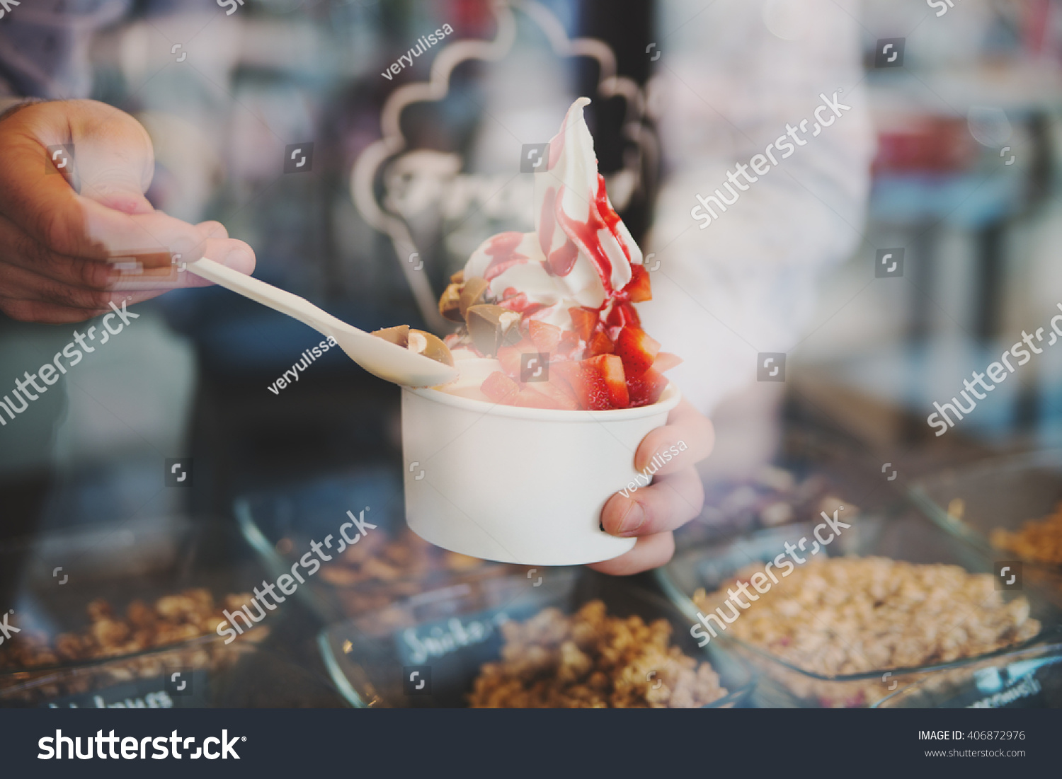 seller pours sauce on a soft frozen yoghurt in white take away cup in cafe #406872976