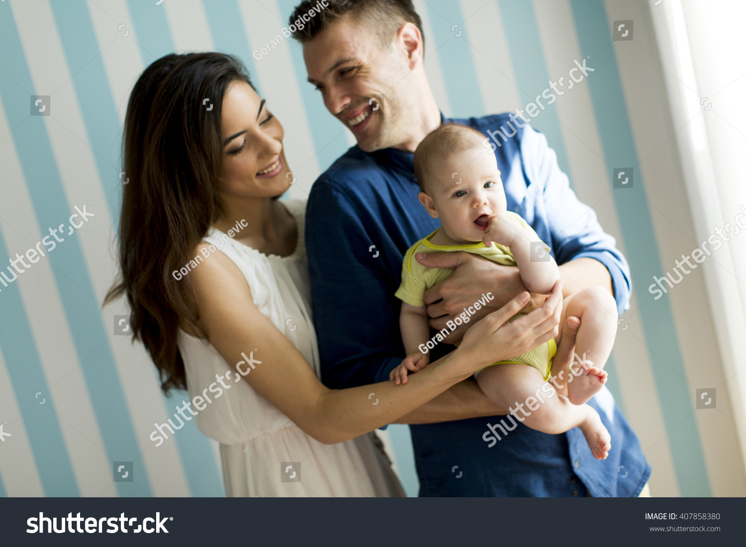 Young family with a baby standing by the wall #407858380
