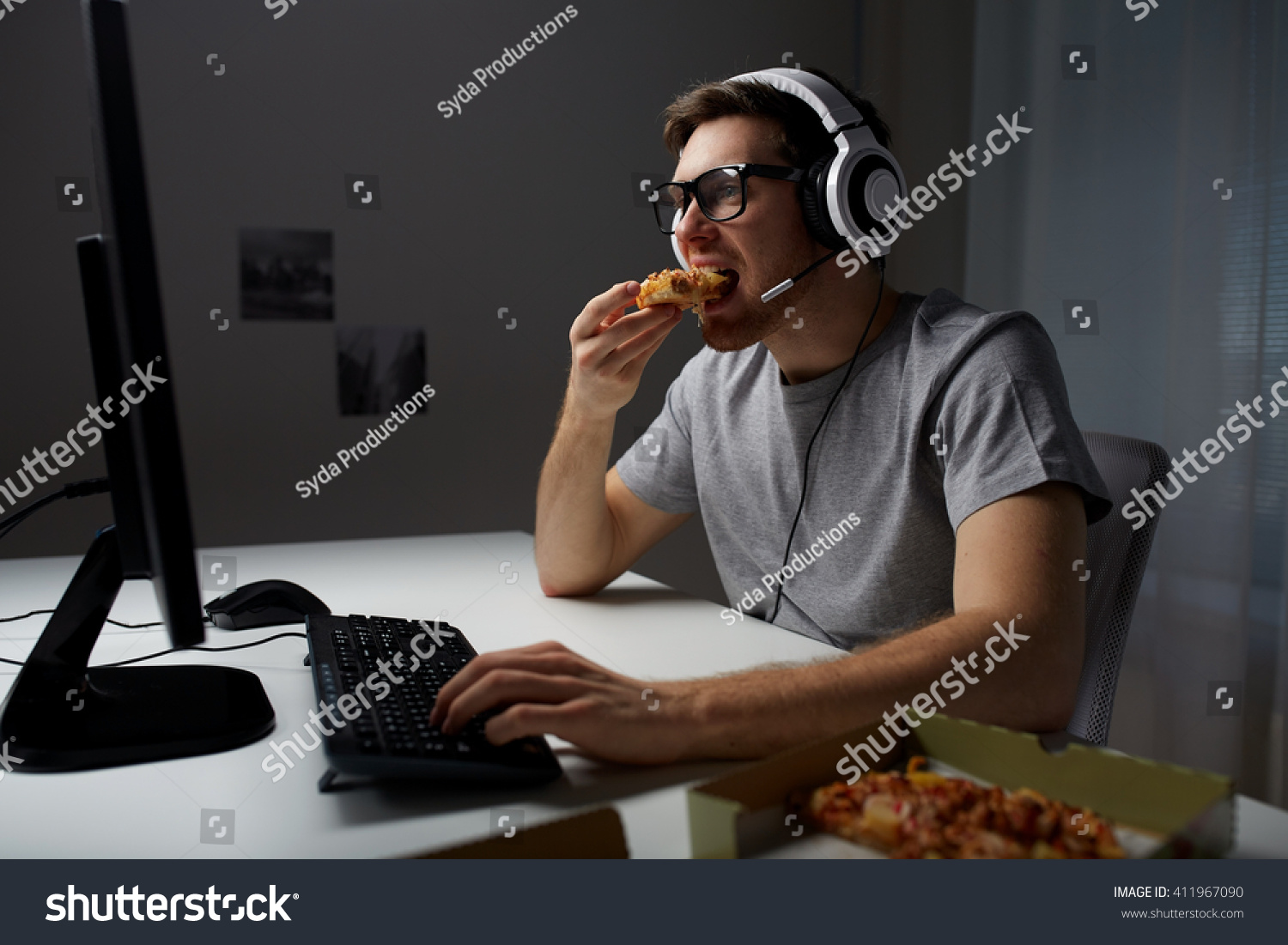 technology, gaming, entertainment, let's play and people concept - young man in headset with pc computer eating pizza while playing game at home and streaming playthrough or walkthrough video #411967090