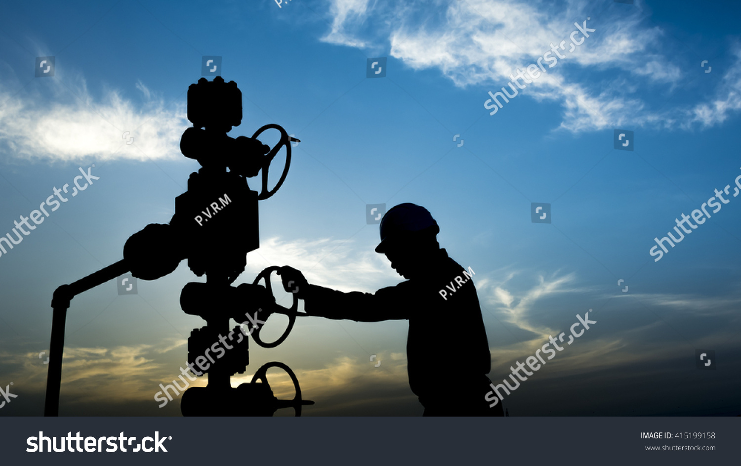 Sunset and silhouette of oilfield worker monitoring wellhead controls in oilfield  #415199158