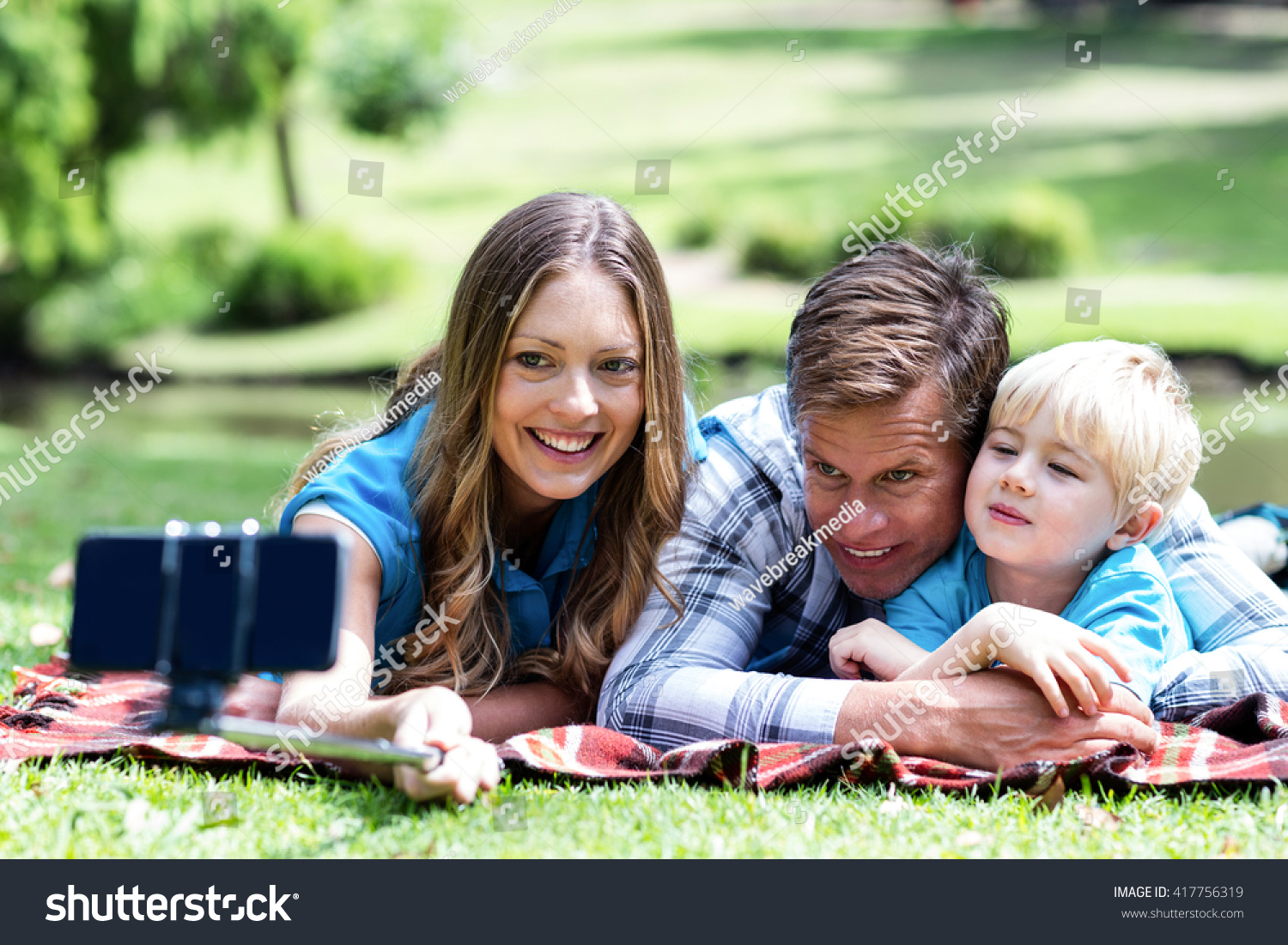 Parents and son taking a selfie on mobile phone with selfie stick in the park #417756319