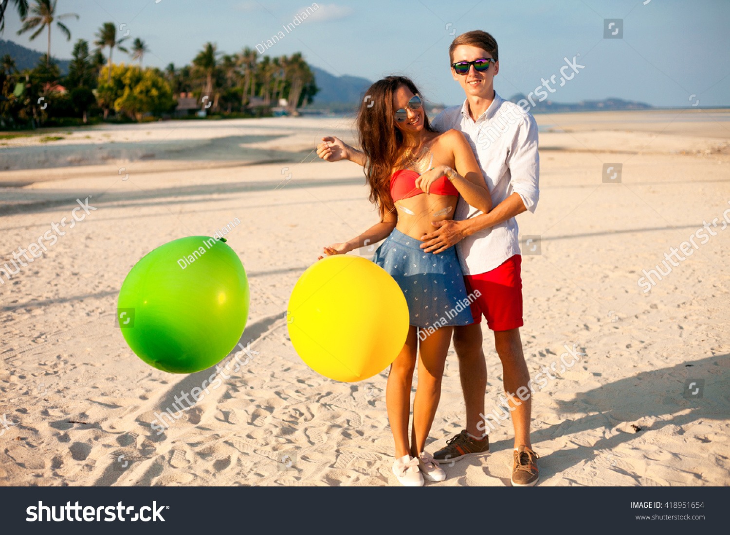 Lovely Portrait of two happy young people dating and having fun on the beach.handsome man make surprise for his Girl,holding her man and  keeping color balloons in hand.Summer beach background.Outdoor #418951654