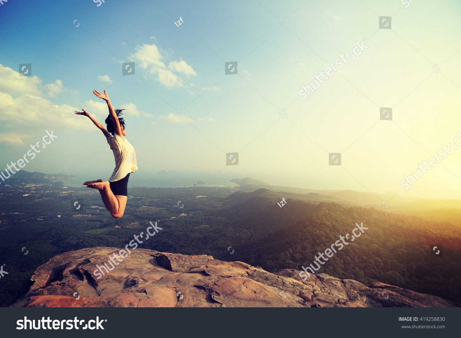cheering happy young asian woman jumping on mountain peak cliff edge #419258830