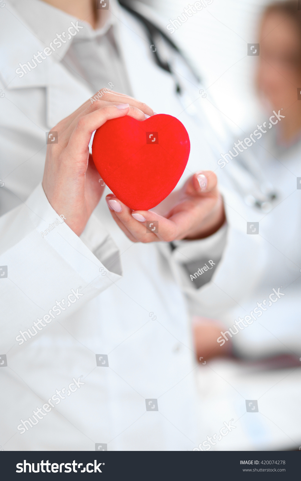 Female doctor with stethoscope holding heart.  Patients couple sitting in the background #420074278