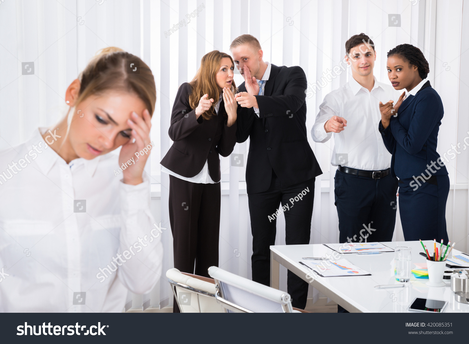 Businesspeople Gossiping Behind Stressed Female Colleague In Office #420085351