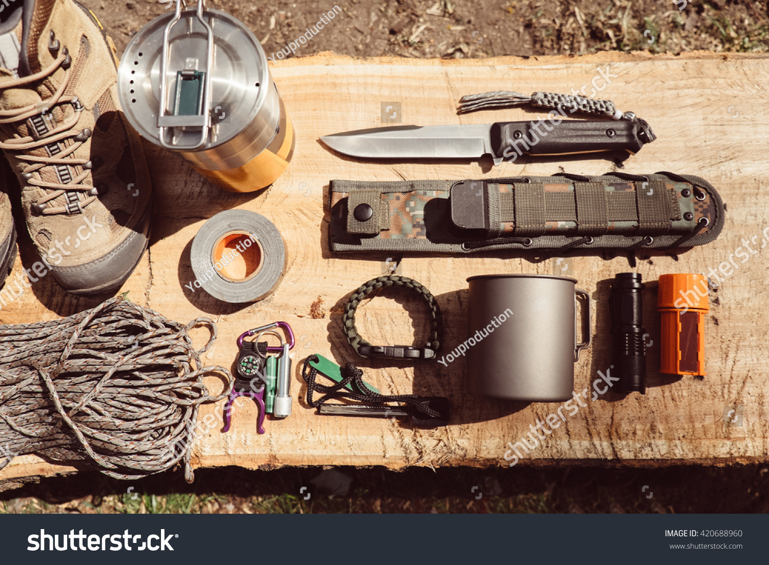 Overhead top view of hiking travel gear on wood log. Items include hiking boots, cup, rope, knife, matches, flashlight, compass. Flat lay of outdoor travel equipment items for mountain camping trip. #420688960
