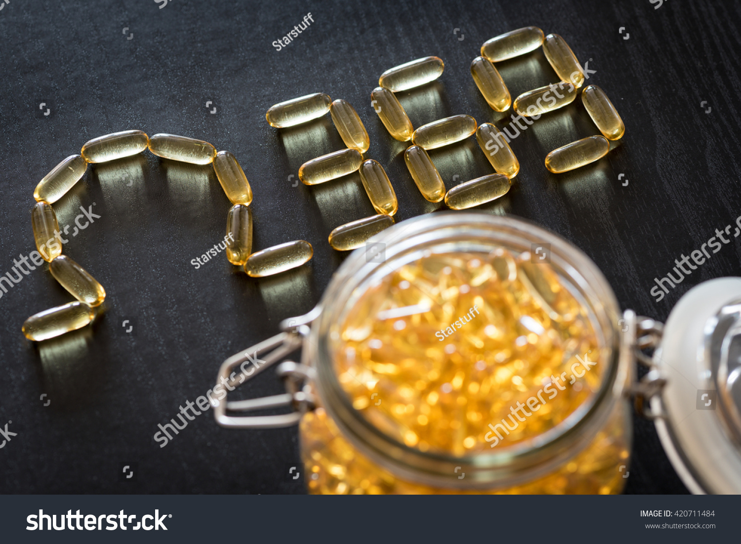 Omega 3-6-9 fish oil yellow softgels drawing omega 3-6-9  letters on wooden black table. Glass airtight jar. #420711484