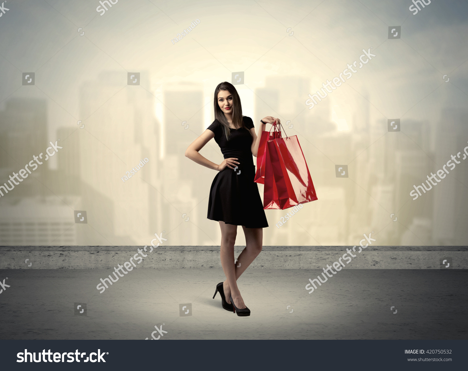 Attractive lady in black holding red shopping bags standing in front o urban landscape with tall buildings concept #420750532