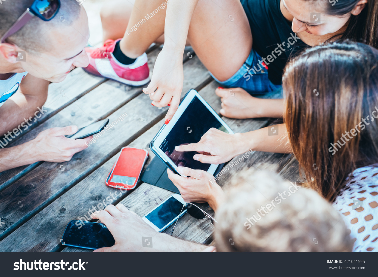 group of young multiethnic friends women and men at the beach in summertime using technological devices smart phone and tablet - social network, technology, communication concept #421041595