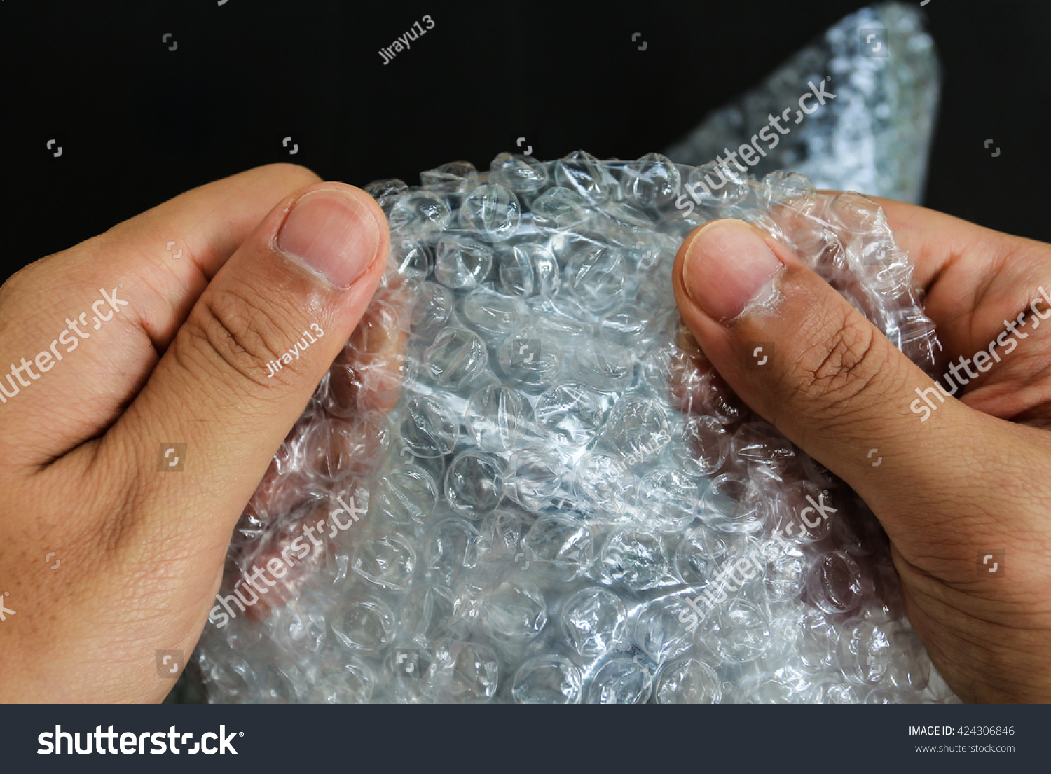 hands popping the bubbles in bubble wrap on black background (selective focus) #424306846