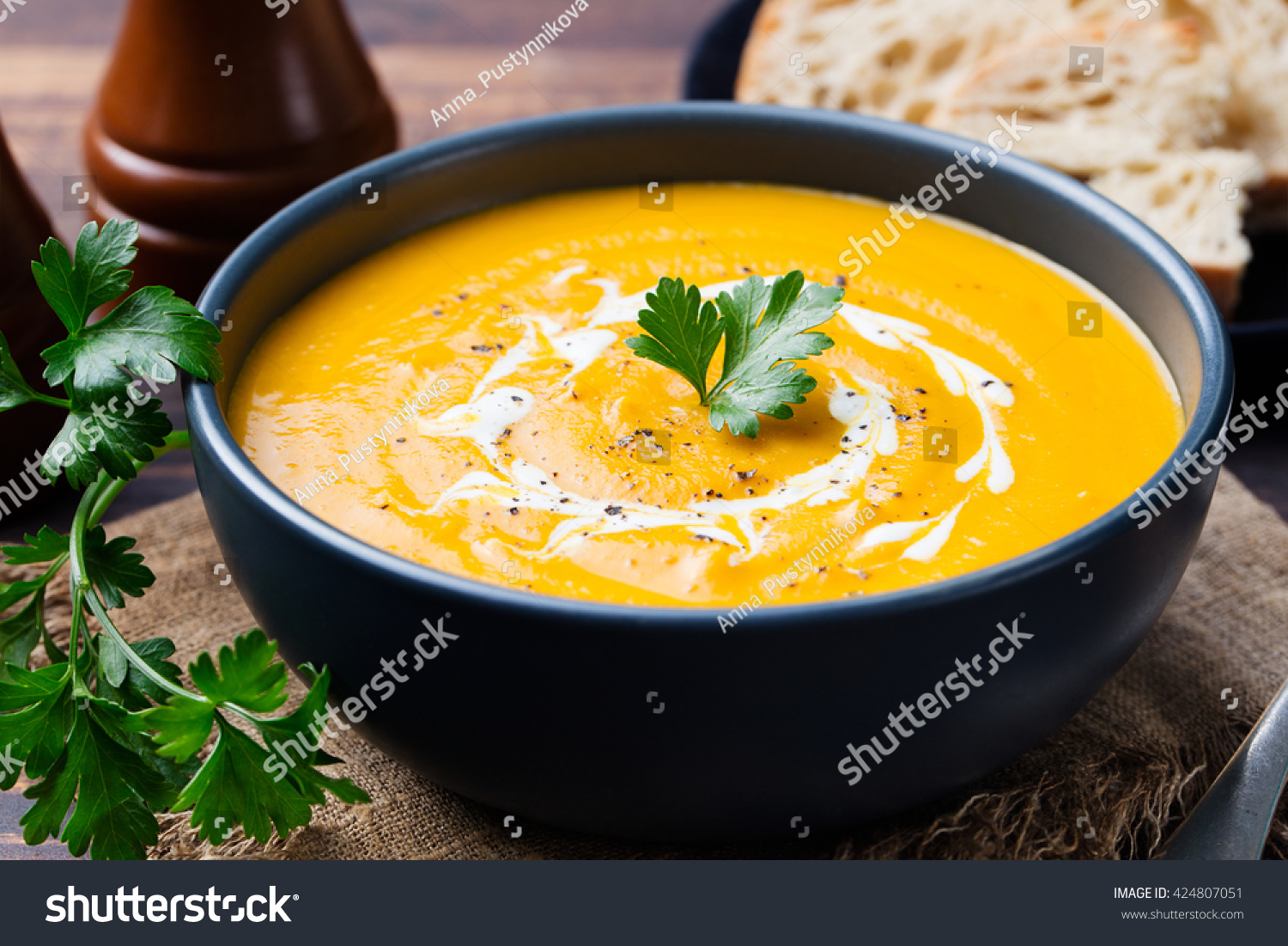 Pumpkin and carrot soup with cream and parsley on dark wooden background #424807051