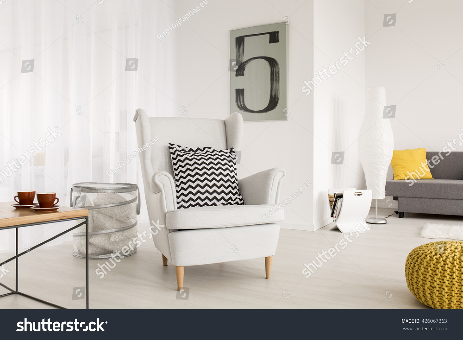 Light living room with simple table and comfortable armchair with decorative pattern pillow #426067363