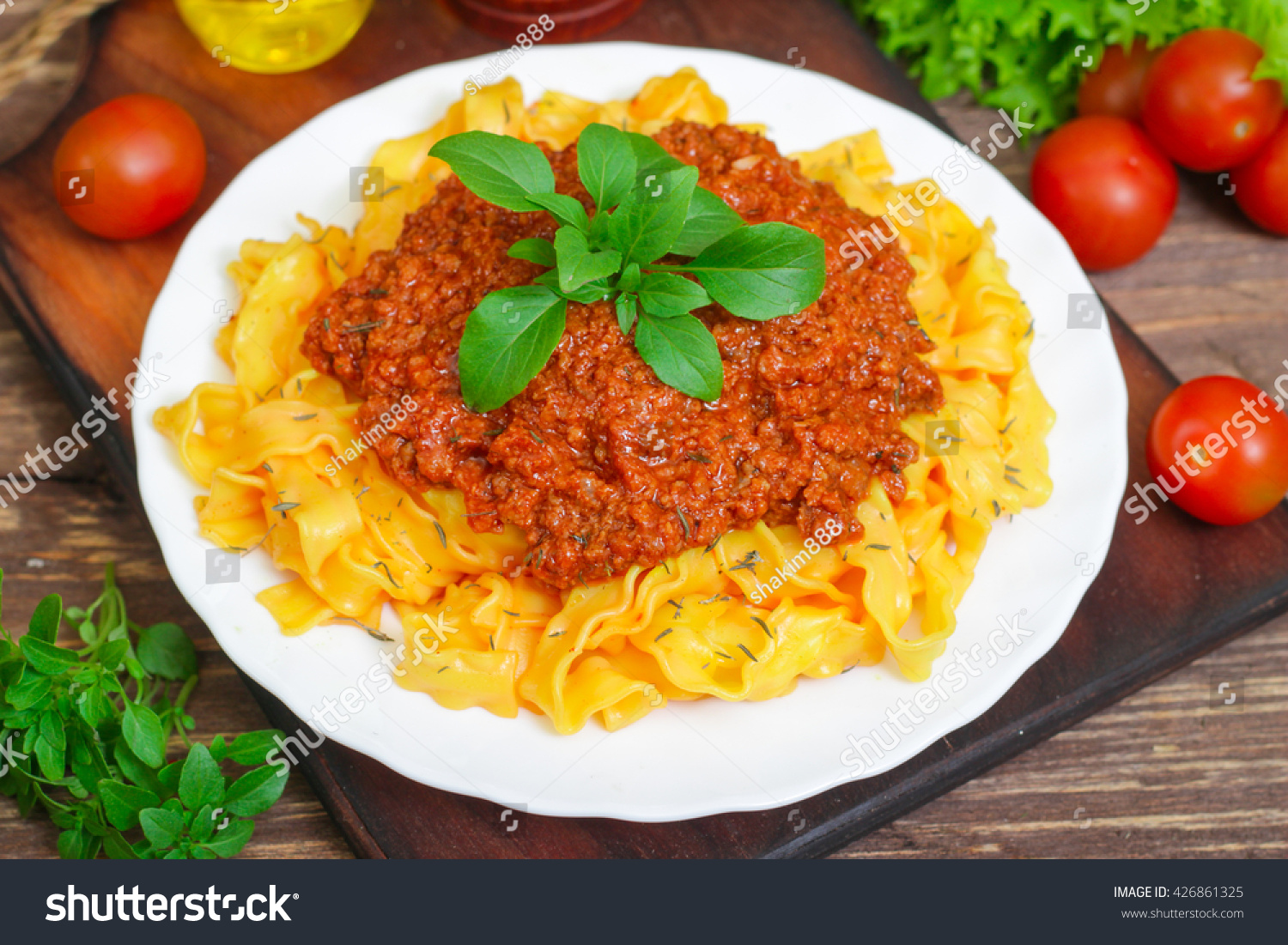 Traditional Italian pasta Bolognese or Bolognese with cooked pasta noodles topped with a spicy tomato based meat sauce garnished with fresh basil on a wooden background #426861325