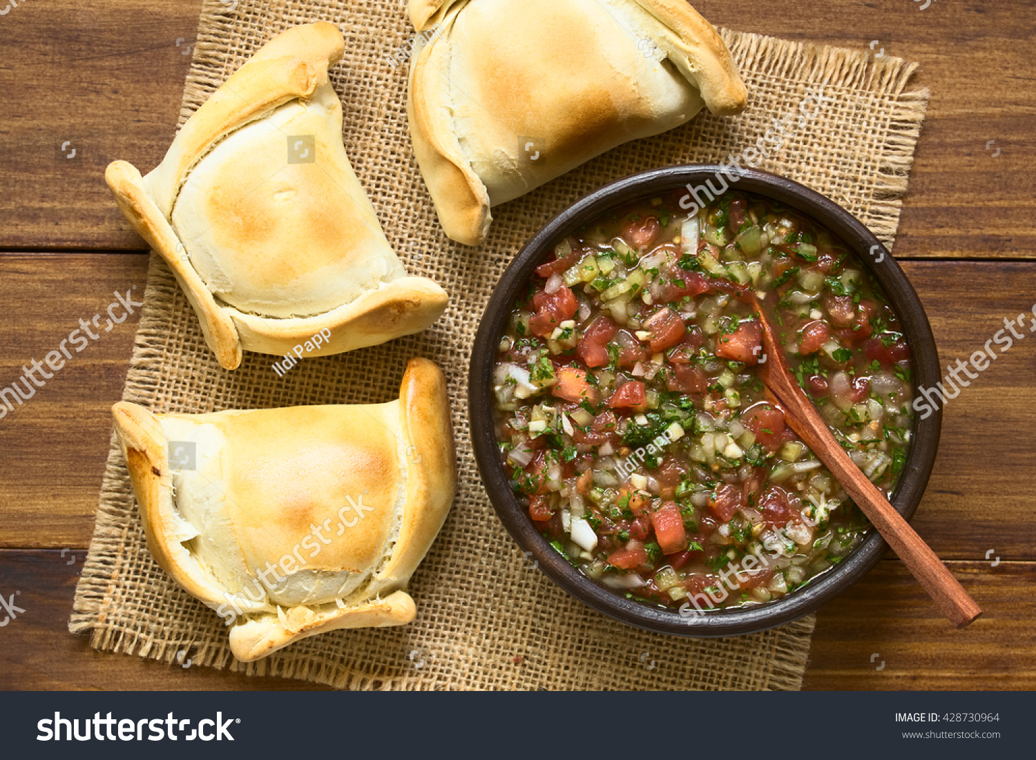 Chilean Pebre sauce, a traditional condiment made of tomato, onion, garlic, spicy aji pepper and coriander with empanadas on the side, photographed overhead on dark wood with natural light #428730964