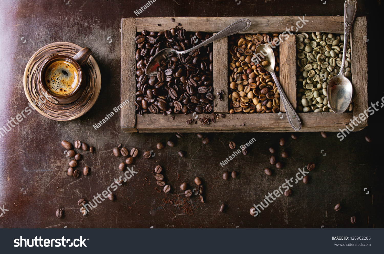 Green and brown decaf unroasted and black roasted coffee beans in old wooden box, and ceramic cup of fresh making coffee over dark brown textured background. Banner top view #428962285
