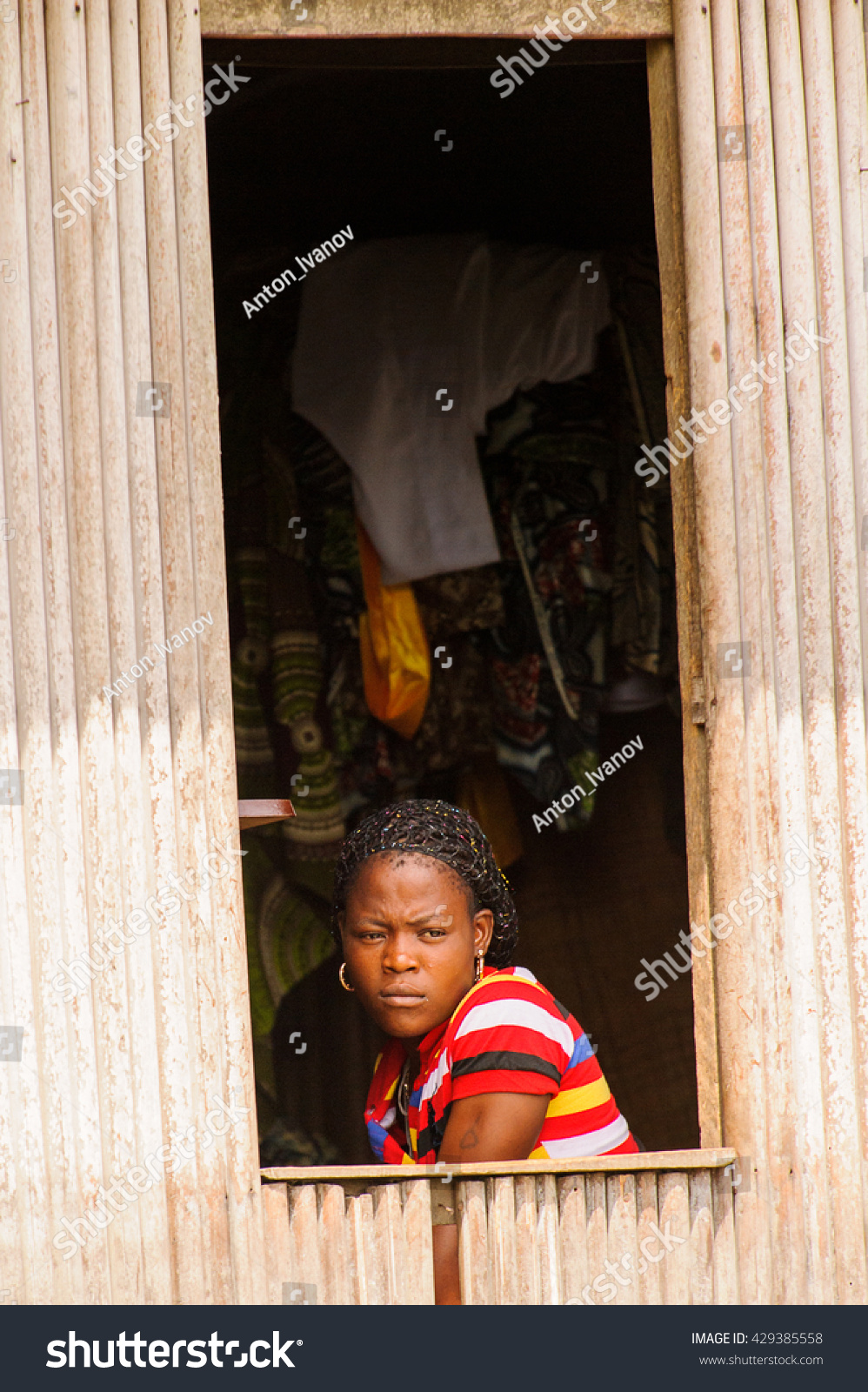PORTO-NOVO, BENIN - MAR 9, 2012: Unidentified Beninese girl looks out of the window. People of Benin suffer of poverty due to the difficult economic situation #429385558