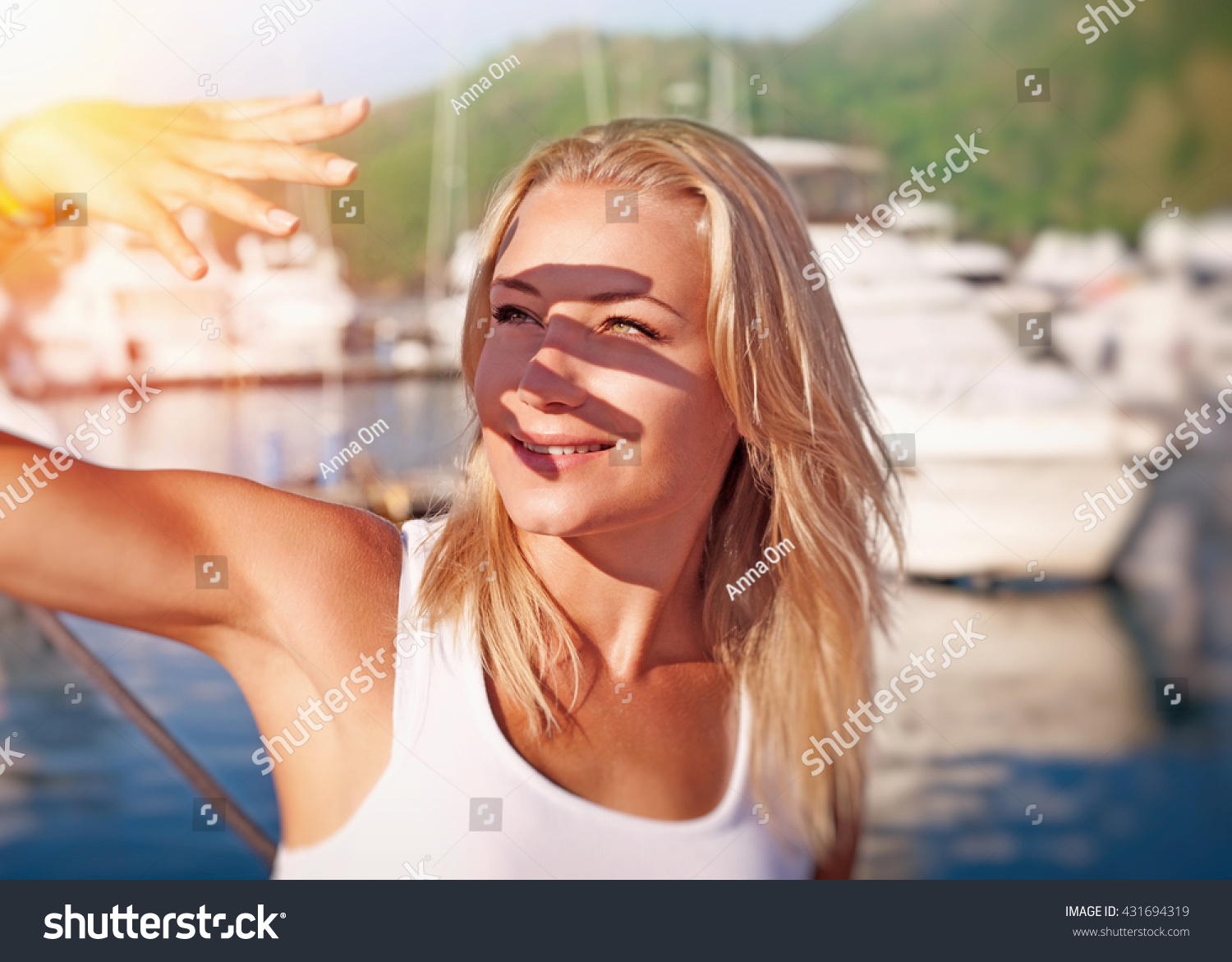 Portrait of a beautiful blond girl covering face by hand of bright sun light, spending weekend on the yacht, happy summer vacation #431694319