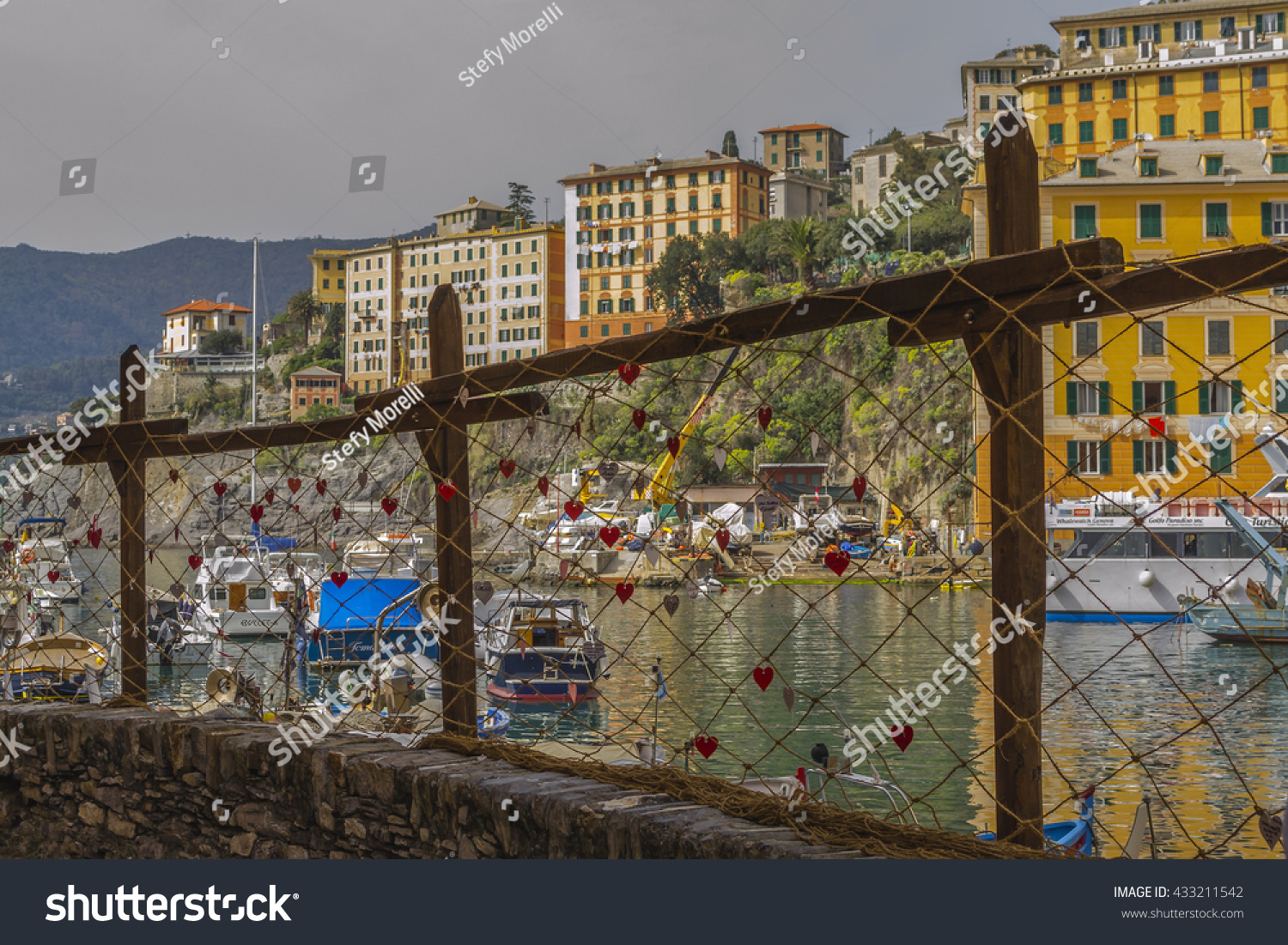 GENOA, LIGURIA, ITALY - April 3, 2016 : Panorama of the port of Camogli seen through a fishing net decorated with red paper hearts. #433211542