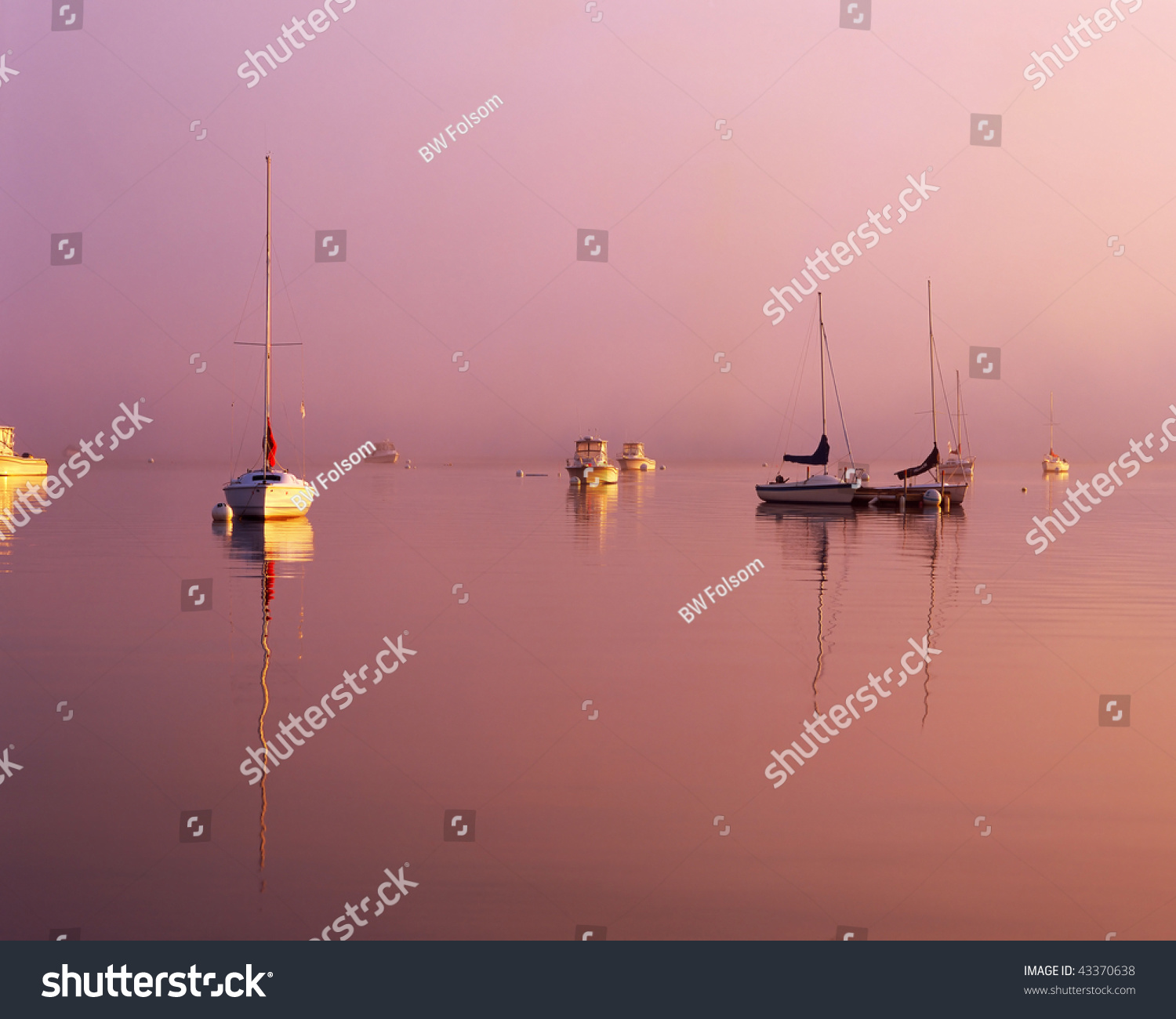 Brilliant sunrise cutting through the morning fog with sailboats at their moorings off the coast of New England #43370638