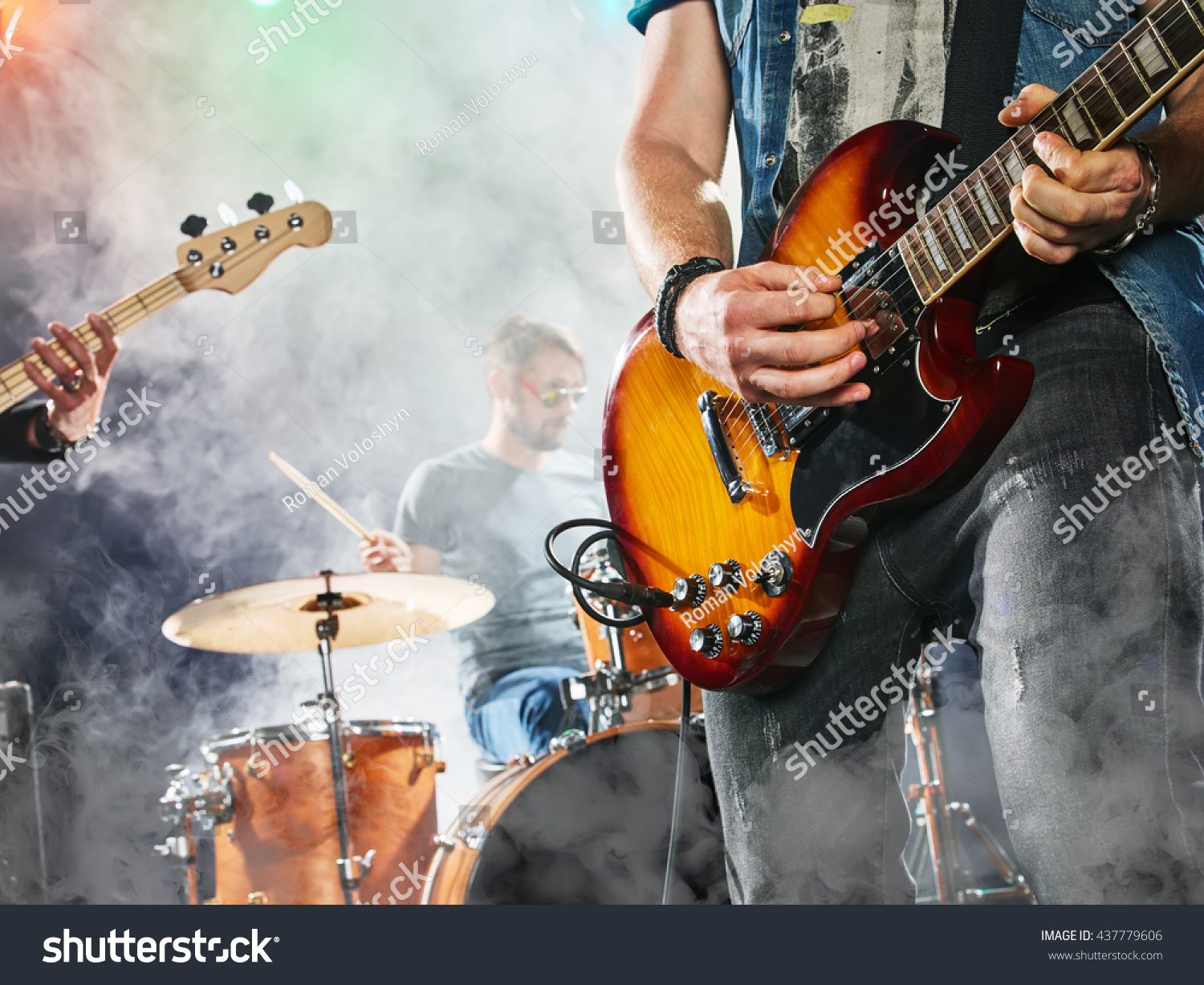 Rock band performs on stage. Guitarist, bass guitar and drums. Guitarist in the foreground. Close-up. #437779606