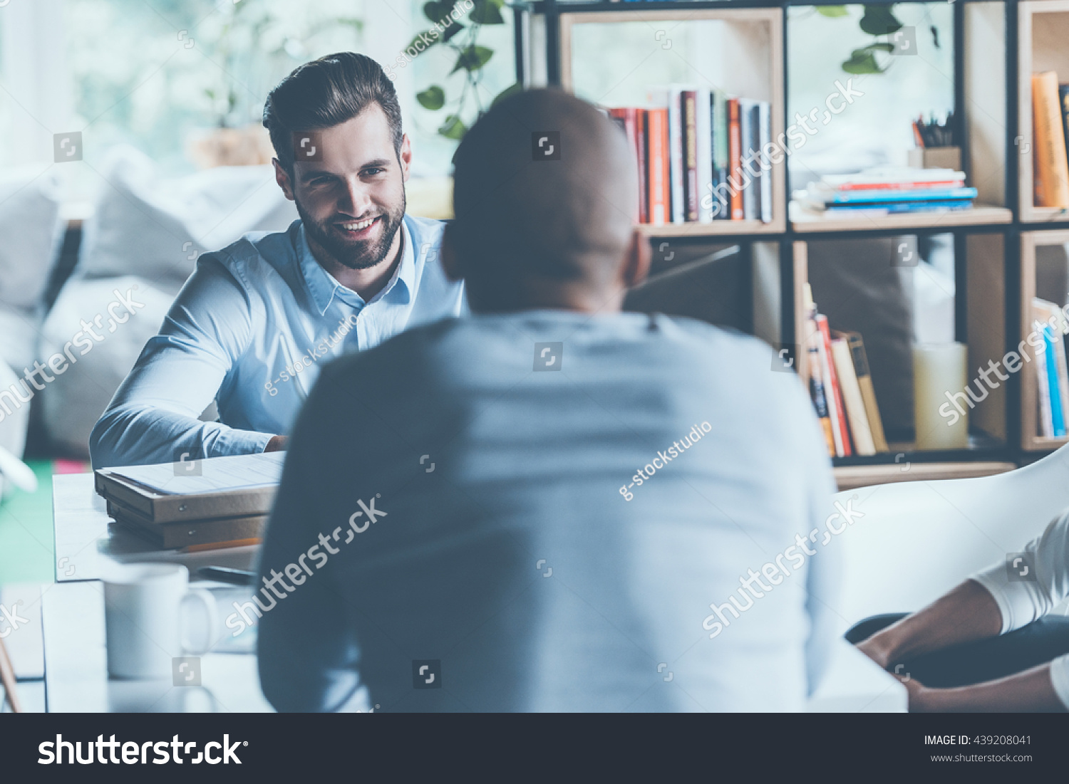 Job interview. Two young men in smart casual wear sitting at the office desk together while one of them smiling  #439208041