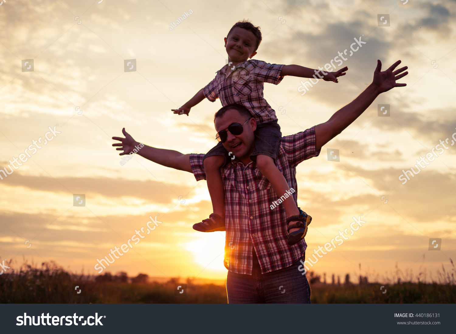 Father and son playing at the park at the sunset time. People having fun on the field. Concept of friendship forever and of summer vacation. #440186131