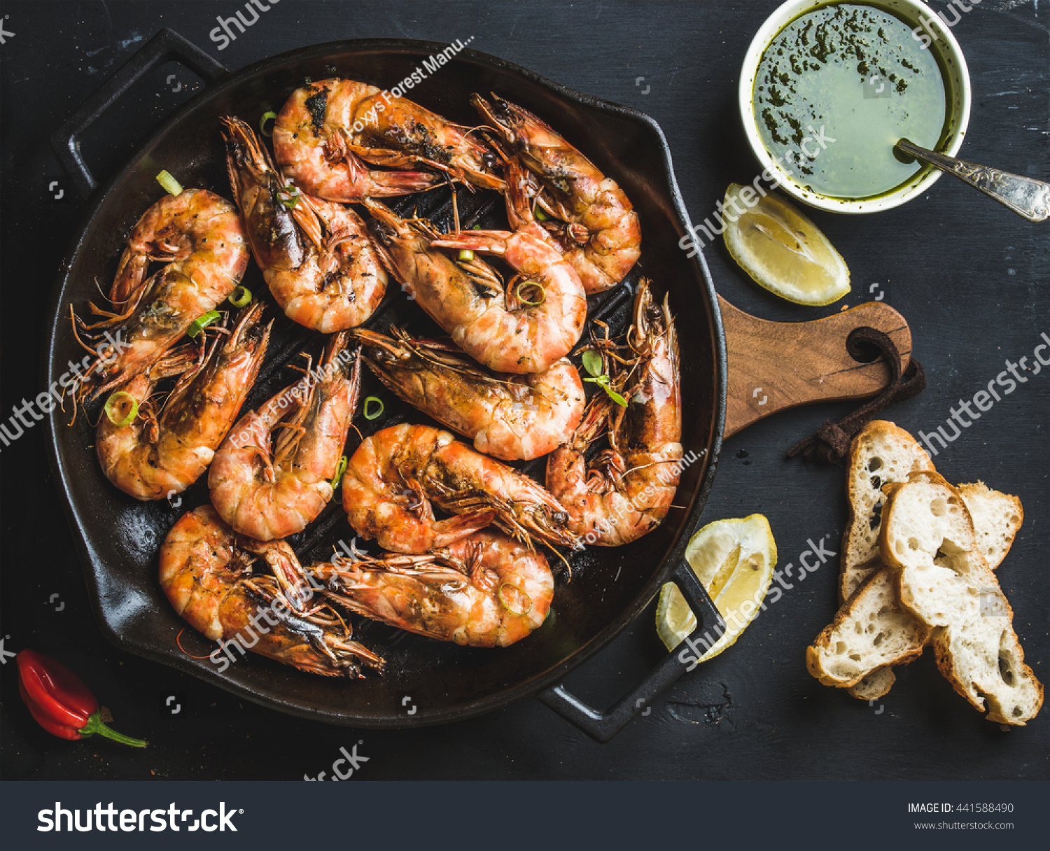 Roasted tiger prawns in iron grilling pan with fresh leek, lemon, bread and pesto sauce over black background, top view #441588490