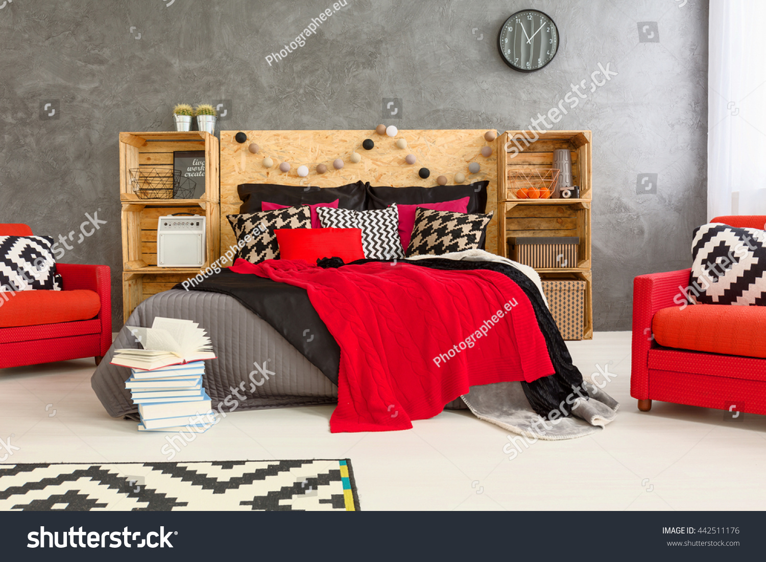 Grey room with double bed with wooden headboard. Red comfortable armchairs and wooden shelves in spacious bedroom #442511176