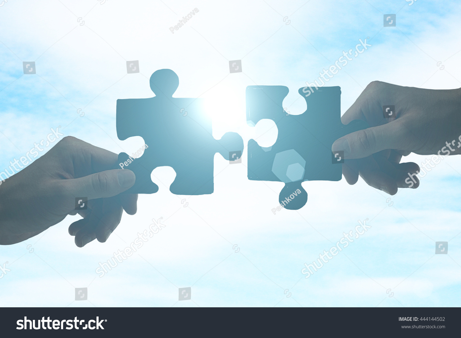 Partnership concept with hands putting puzzle pieces together on sky background with sunlight #444144502