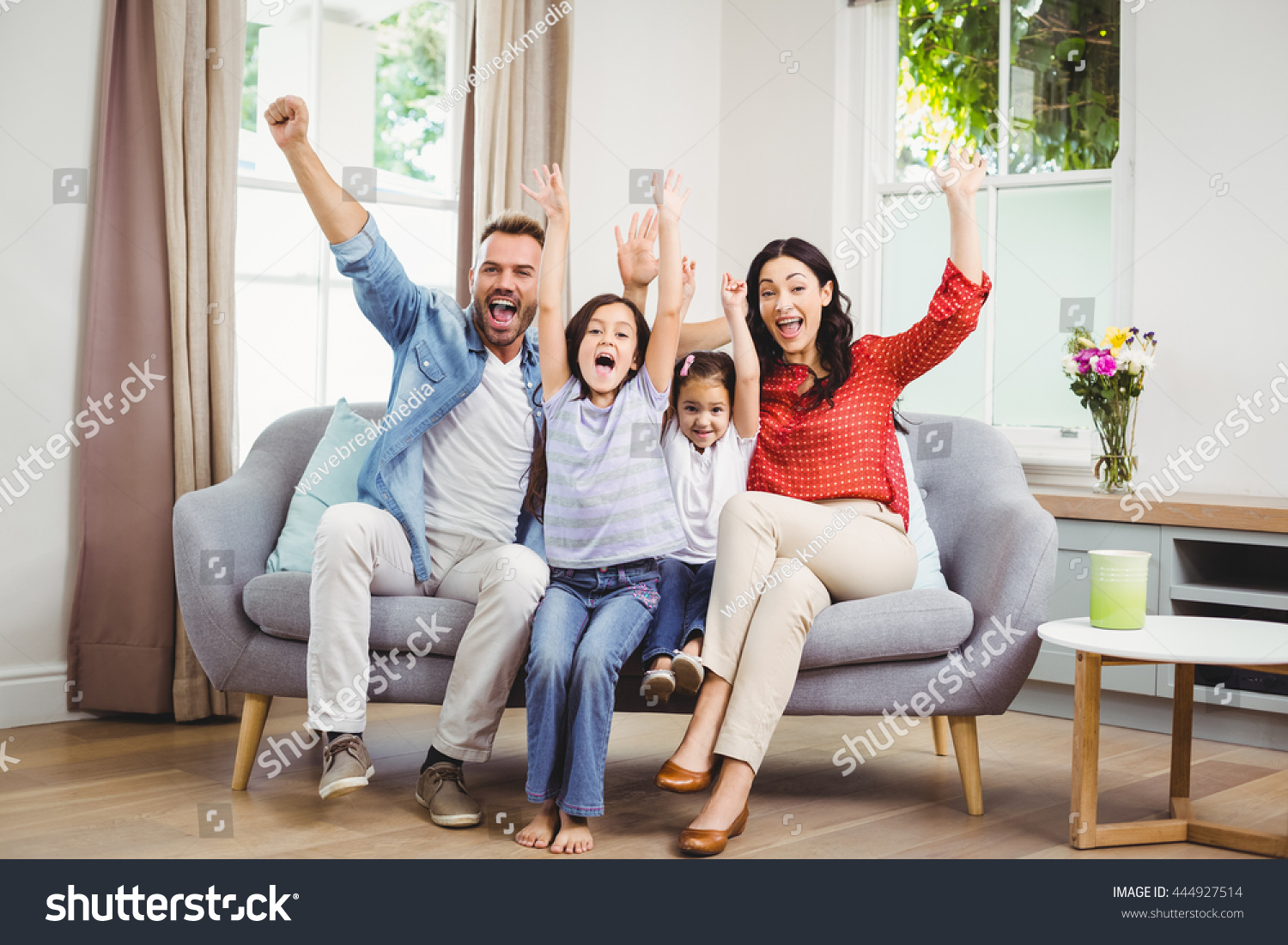 Full length of happy family cheering while siting on sofa at home #444927514