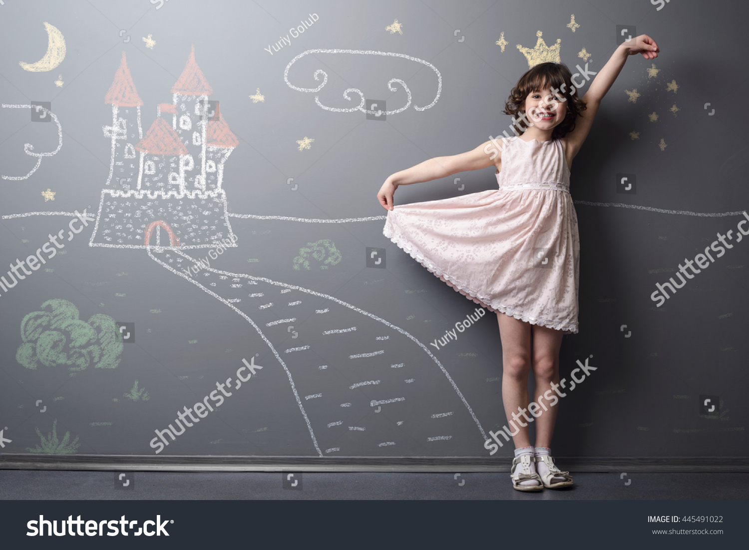 Little princess near her castle smiles and holds her dress with hand. Depicted road, crown and stars on the neutral background. True emotion of happiness of the child. #445491022