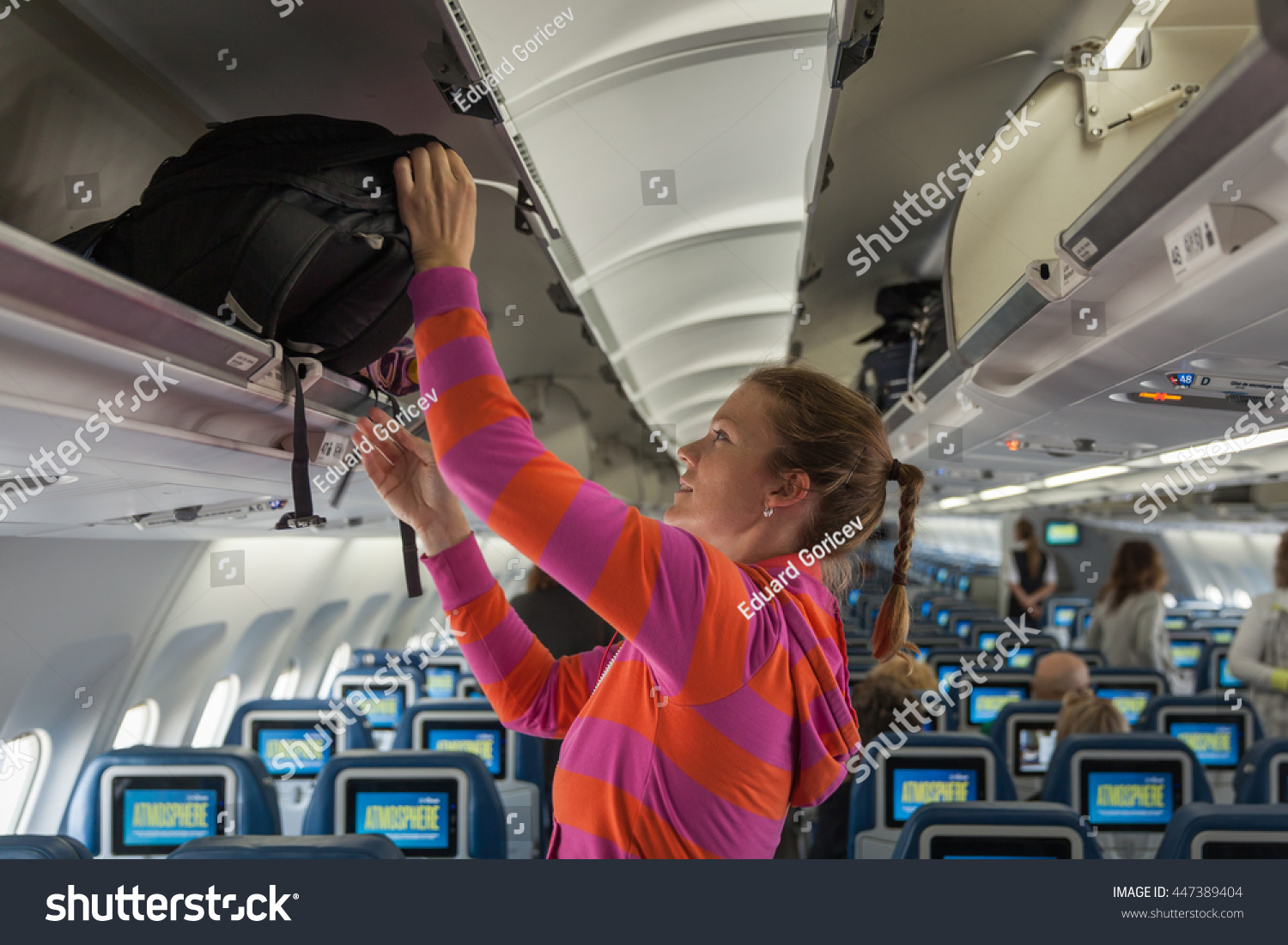 The young girl placed her hand luggage into the compartment on the plane #447389404