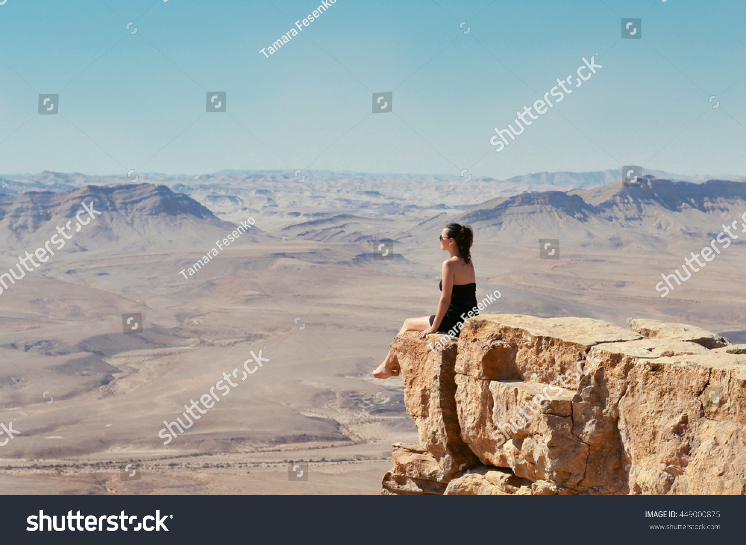 Girl sitting on a cliff and looking at desert Negev landscape. Summer vacation in Israel. #449000875