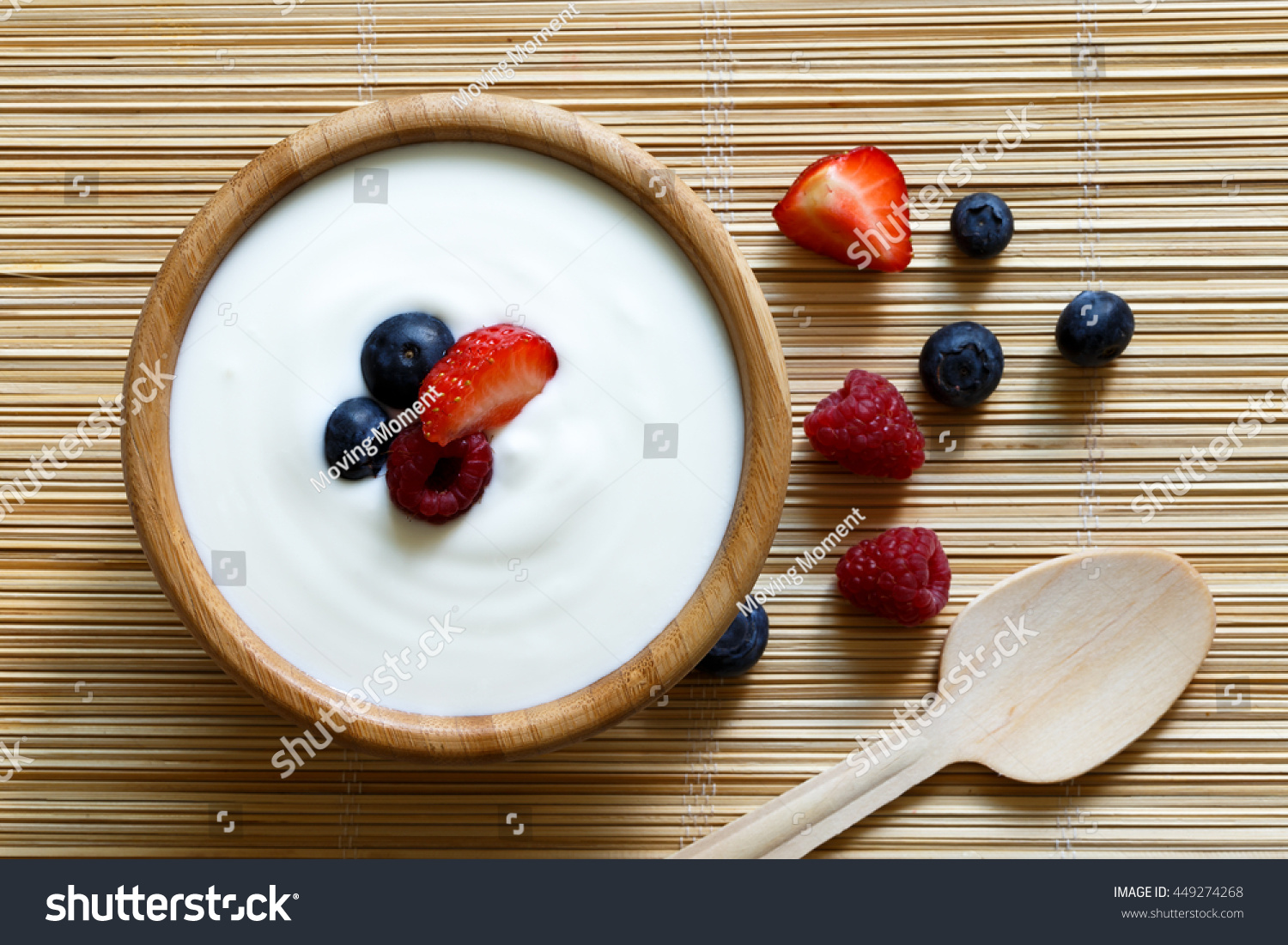 Wooden bowl of white yogurt on bamboo matt from above with wooden spoon. Next to berries. #449274268