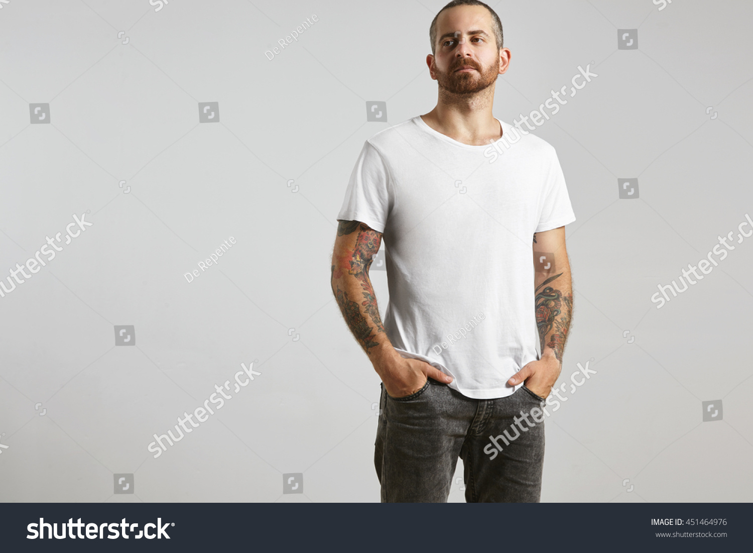 Attractive brutal tattooed bearded guy poses in black jeans and blank white t-shirt from premium thin summer cotton, isolated on white mockup #451464976