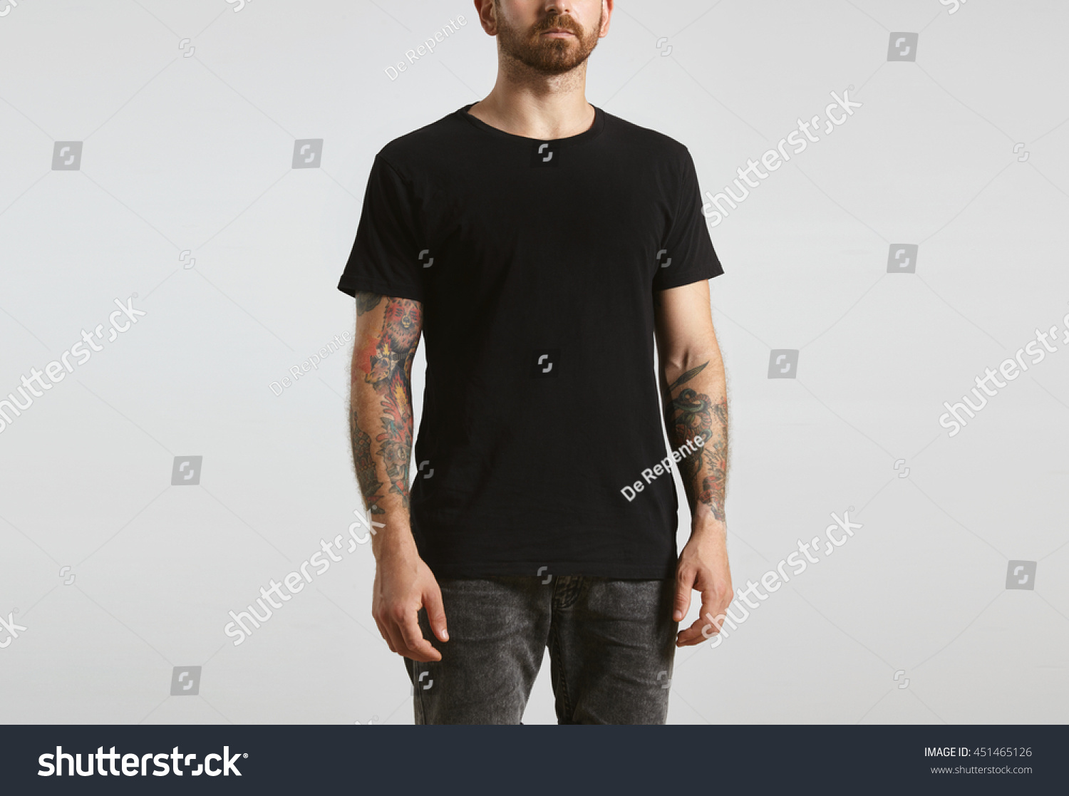 Brutal attractive bearded biker man with tattooed hands poses in black blank t-shirt from premium thin cotton, isolated on white mockup #451465126