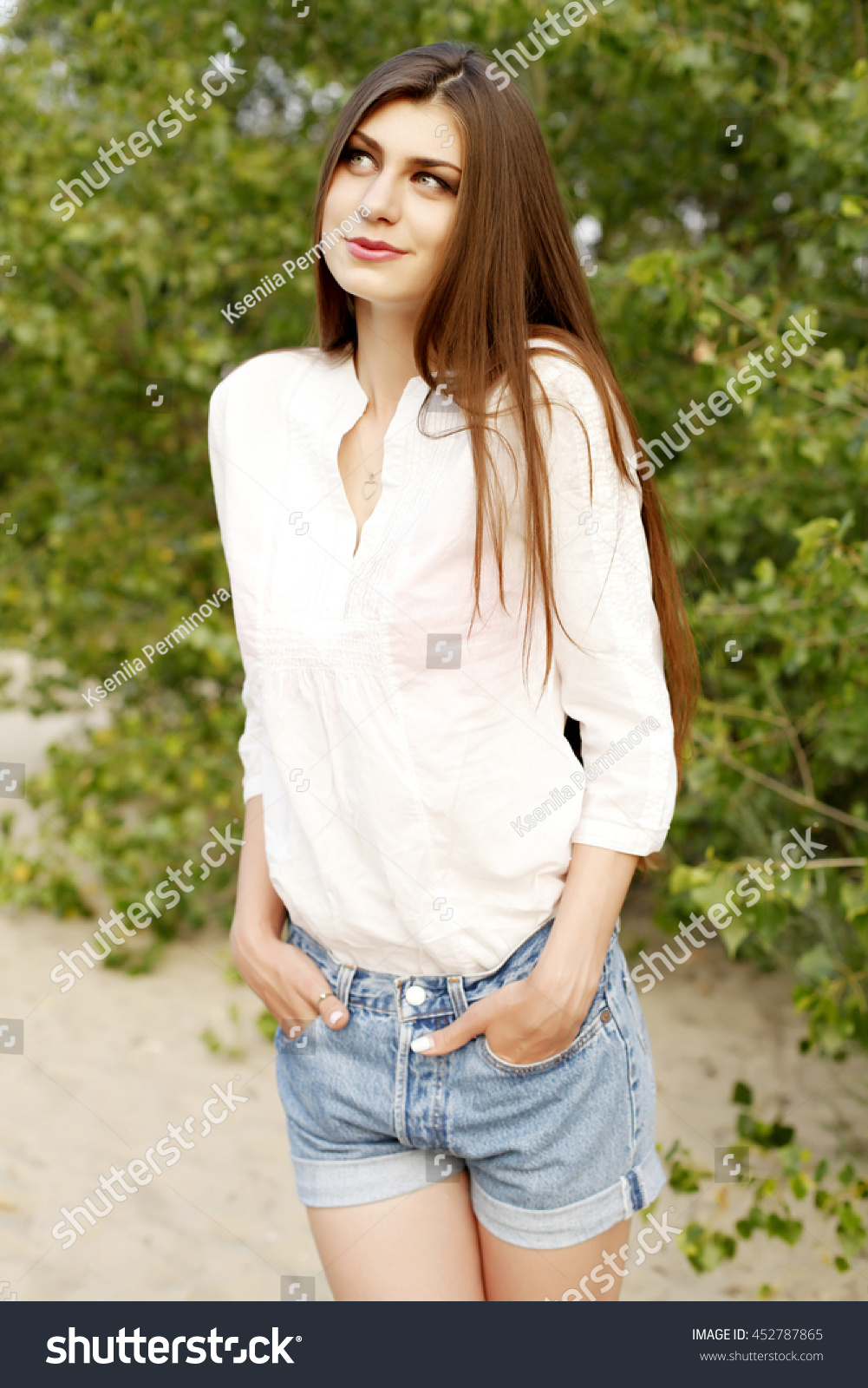 Young beautiful stylish girl with long healthy hair in white blouse and jeans shorts walking and posing in the park. Outdoors, lifestyle #452787865