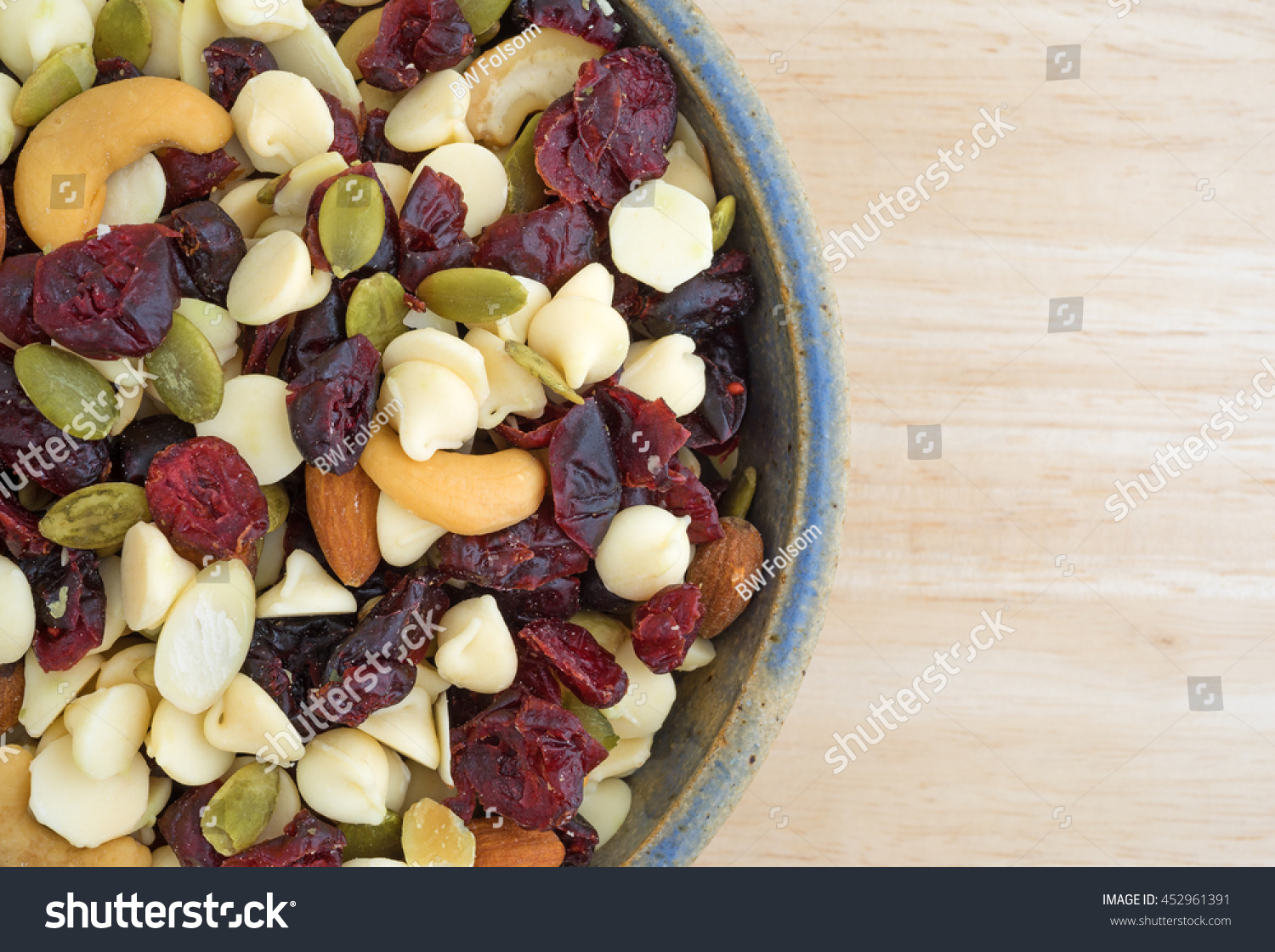 Top close view of a bowl full of an assortment of nuts and dried cranberries trail mix on a wood table top. #452961391