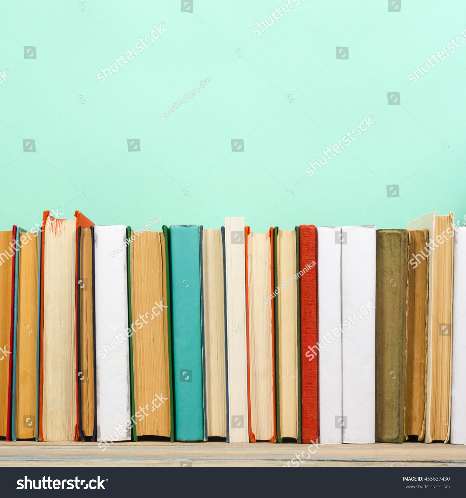 Stack of colorful books, mint green background, free copy space Vintage old hardback books on wooden shelf on the deck table, no labels, blank spine. Back to school. Education green background #455637430