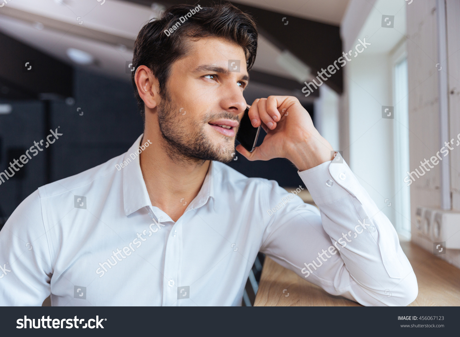 Attractive young businessman sitting and talking on mobile phone sitting indoors in cafe #456067123